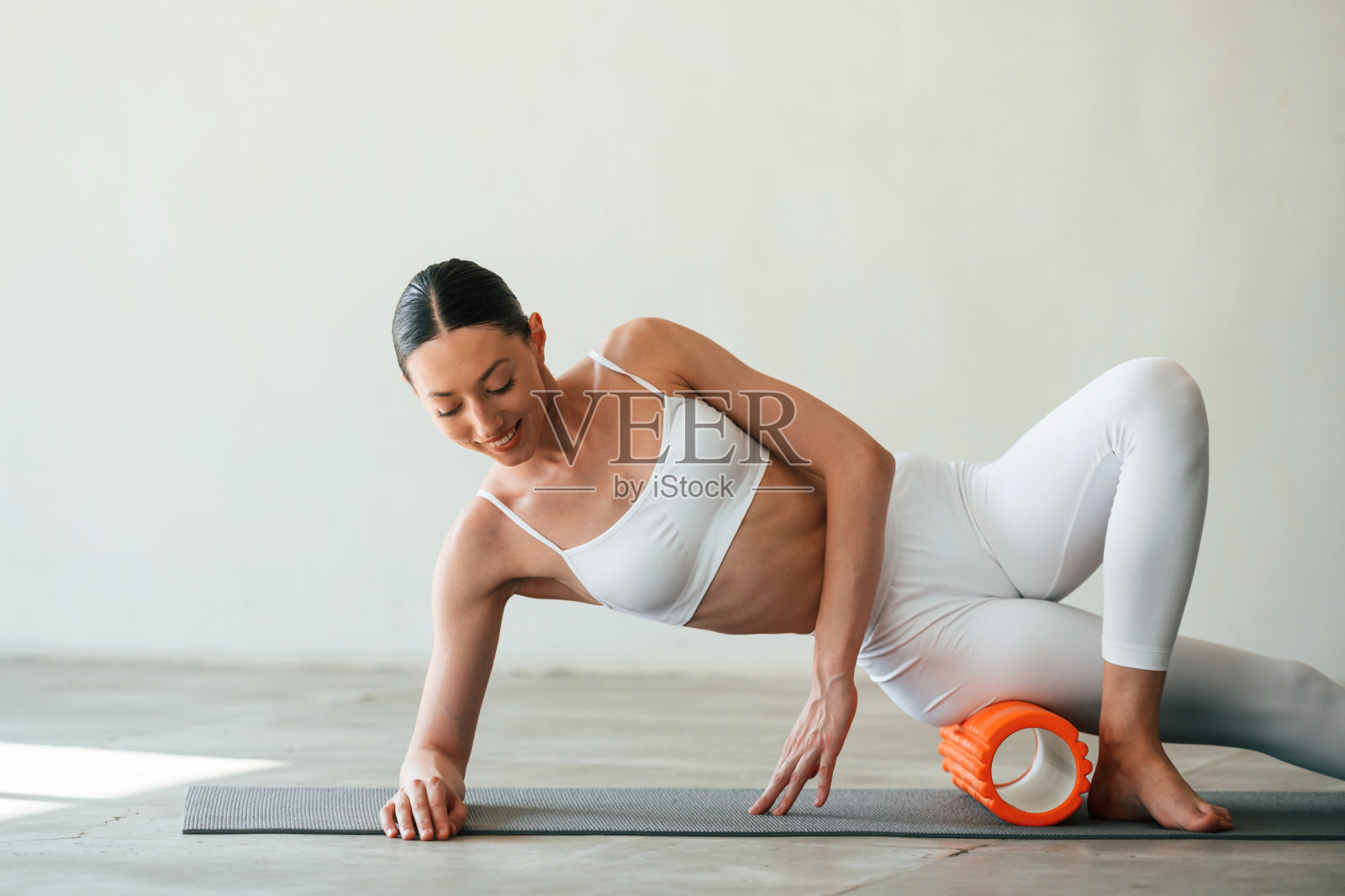 使用泡沫滚筒进行锻炼。身材苗条的年轻女子在演播室里穿着健身服照片摄影图片