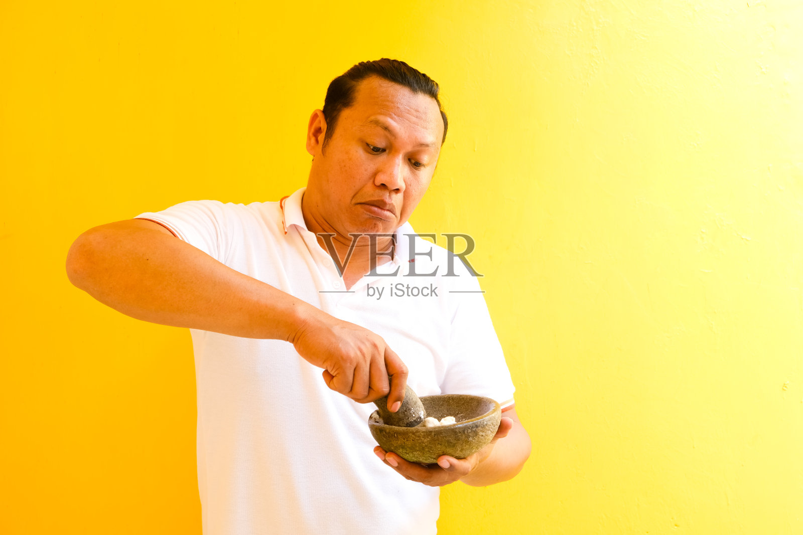 一个亚洲人用黄色背景的研钵研磨烹饪用的香料照片摄影图片