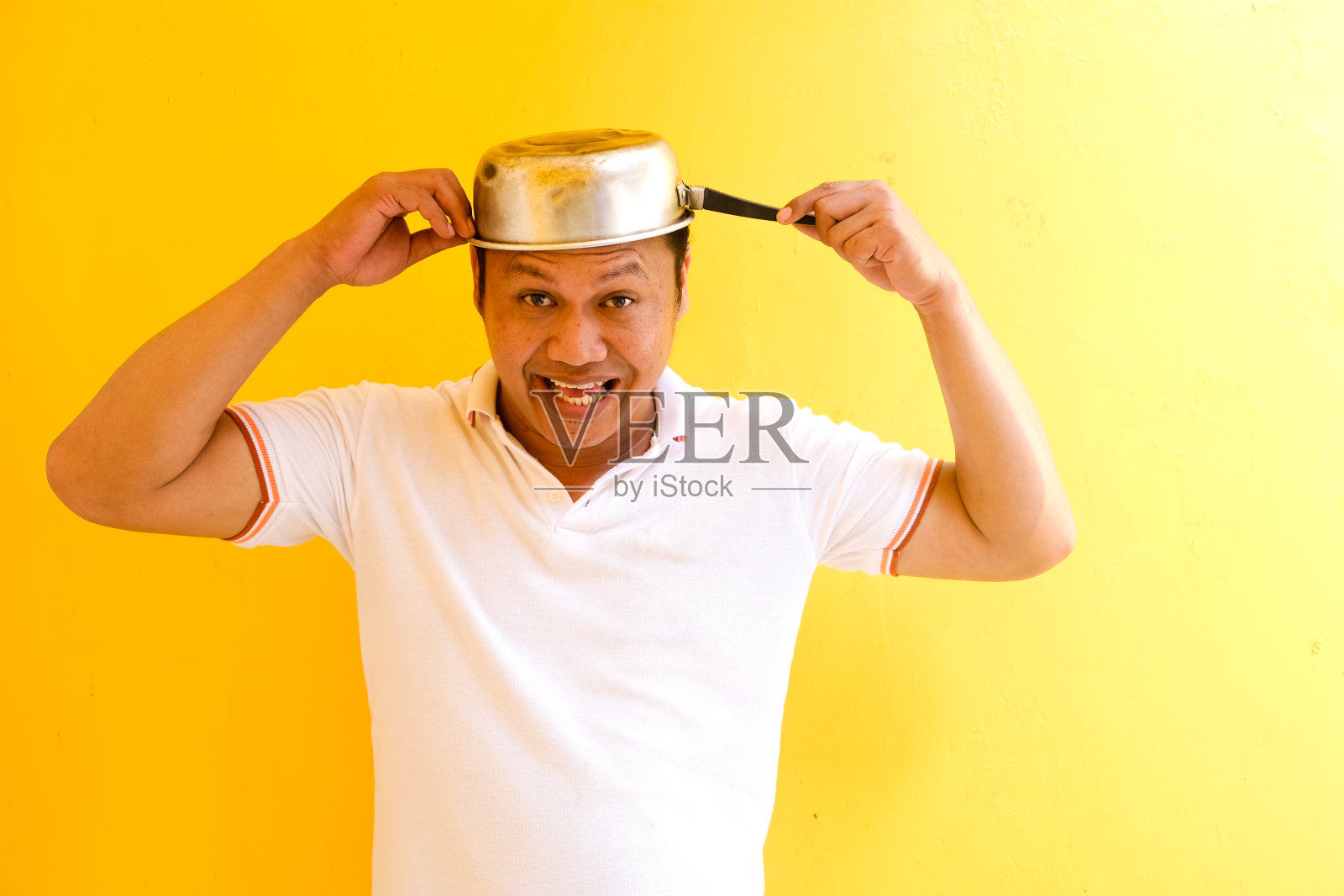 面带微笑的亚洲男子头戴平底锅，孤立的黄色背景照片摄影图片