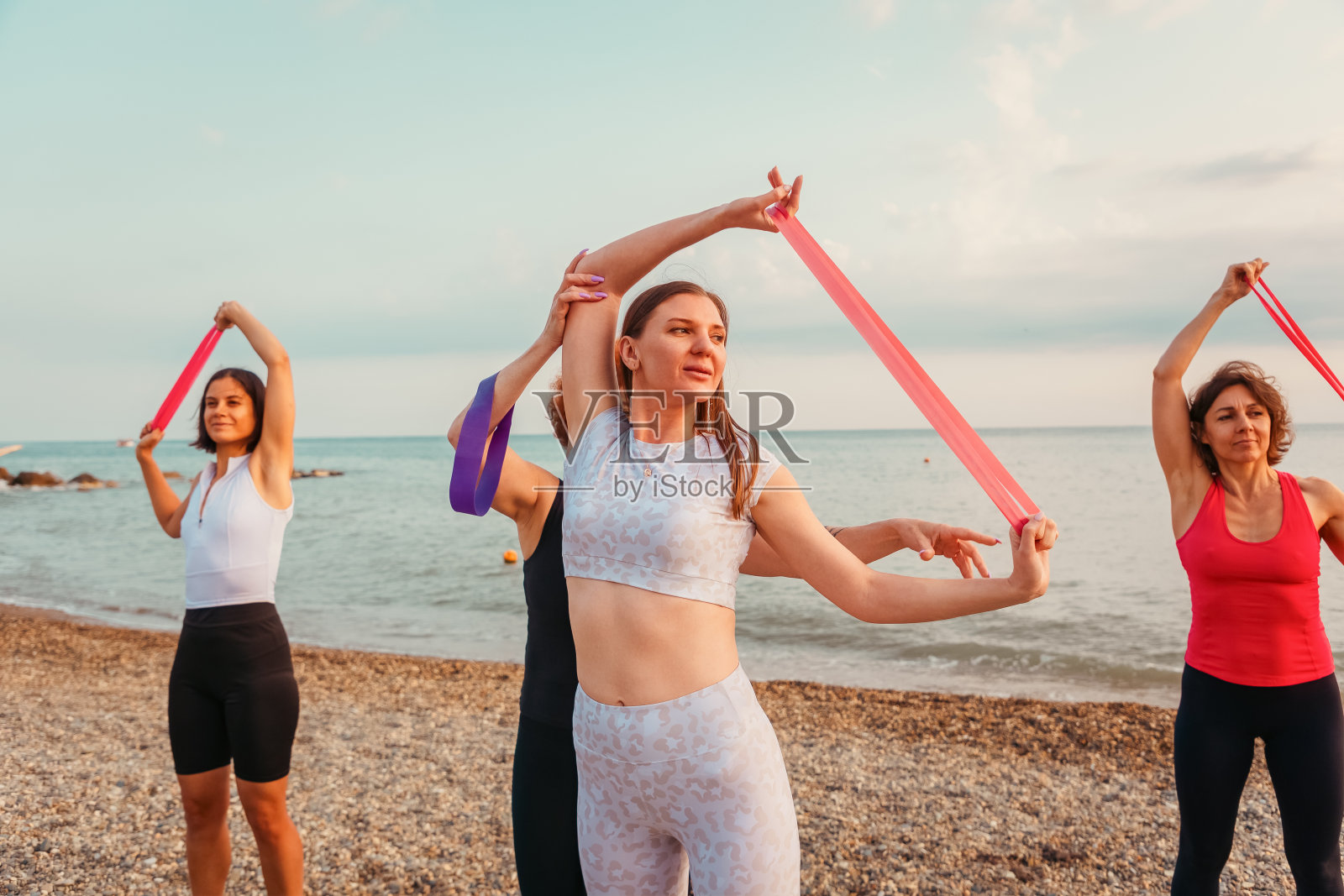 一群白种成年妇女正在沙滩上做运动和伸展运动。健康生活方式及户外训练理念照片摄影图片