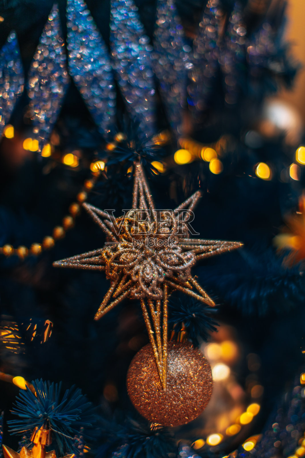 蓝色的圣诞树树枝上挂着金色的圣诞星星。照片摄影图片