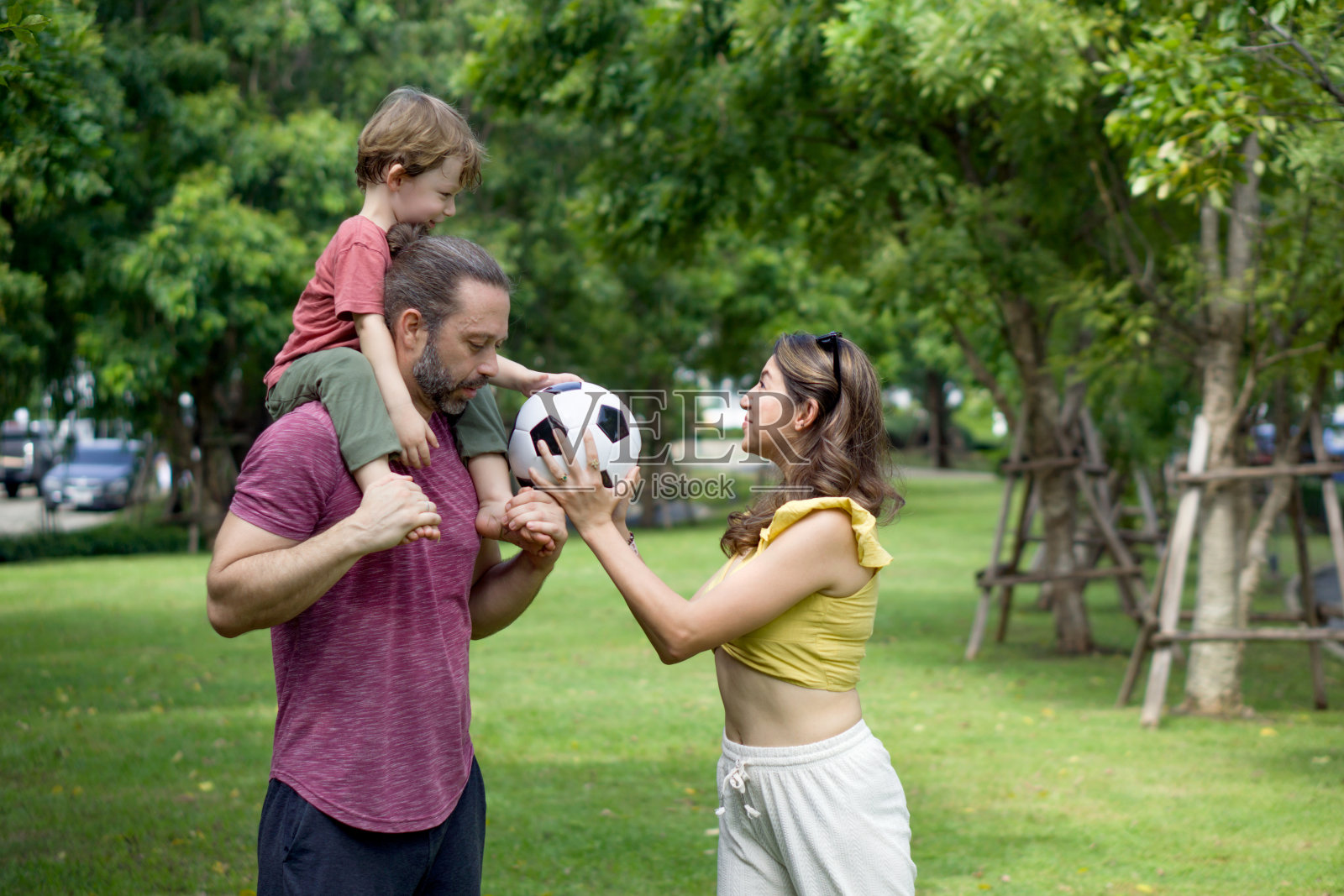 一个快乐的家庭在郁郁葱葱、宁静的公园里进行着一场有趣的足球比赛，充满了欢乐和笑声。照片摄影图片