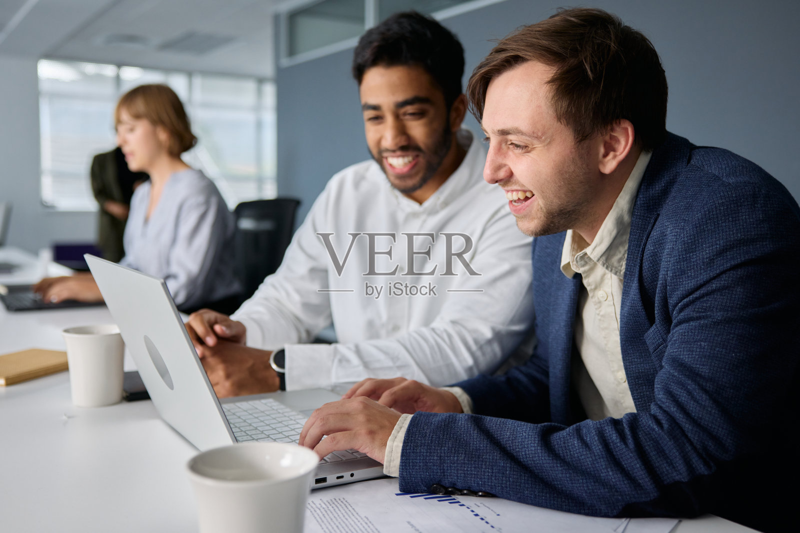 四个快乐的年轻多种族商人，穿着职业装，在办公室的办公桌前用笔记本电脑工作照片摄影图片