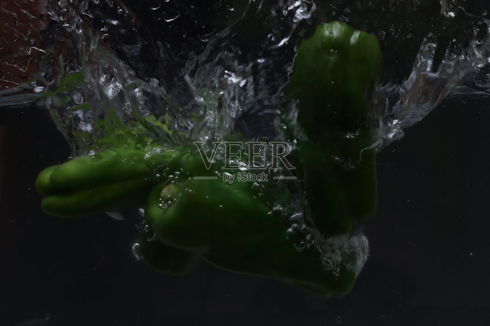 青椒落入水中，黑色背景上溅起水花。照片摄影图片