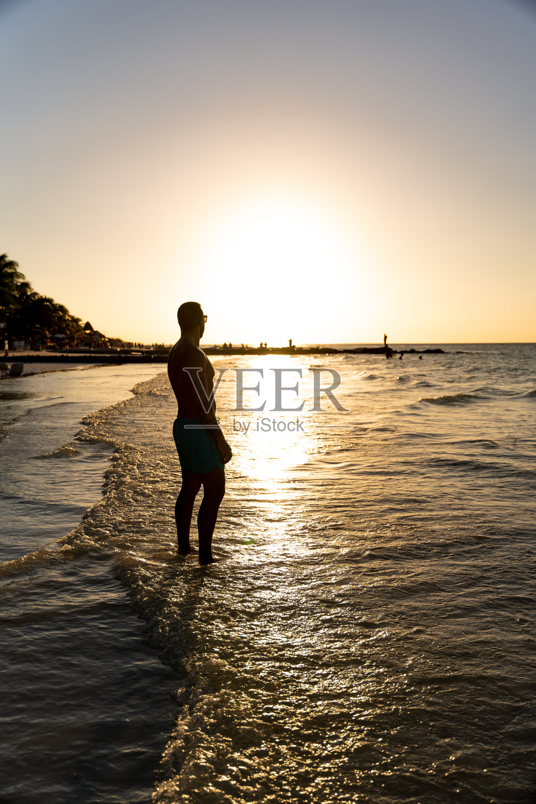 日落时分，一个无法辨认的年轻人站在霍尔博克斯海滩的岸边，正在墨西哥度假。照片摄影图片