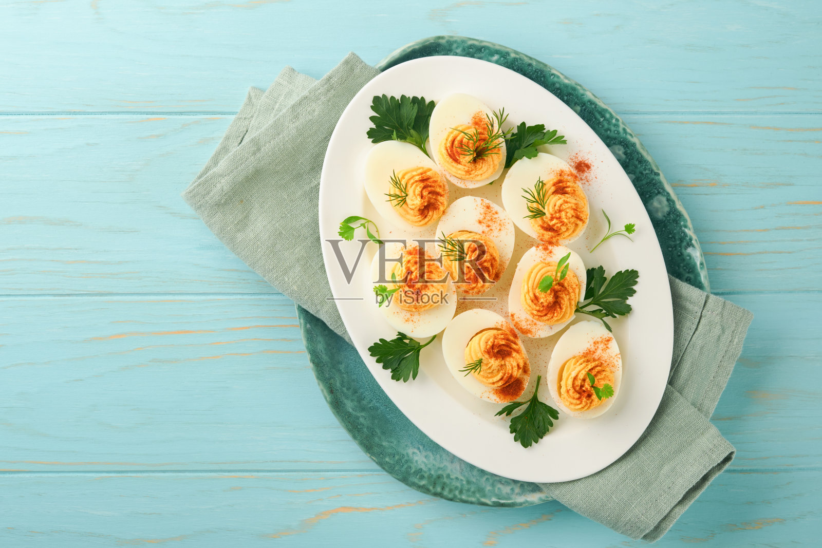 复活节餐桌上用蓝盘子盛上红辣椒和欧芹馅蛋或魔鬼蛋。复活节的传统菜肴。早餐要吃健康的食物。俯视图，平铺。照片摄影图片