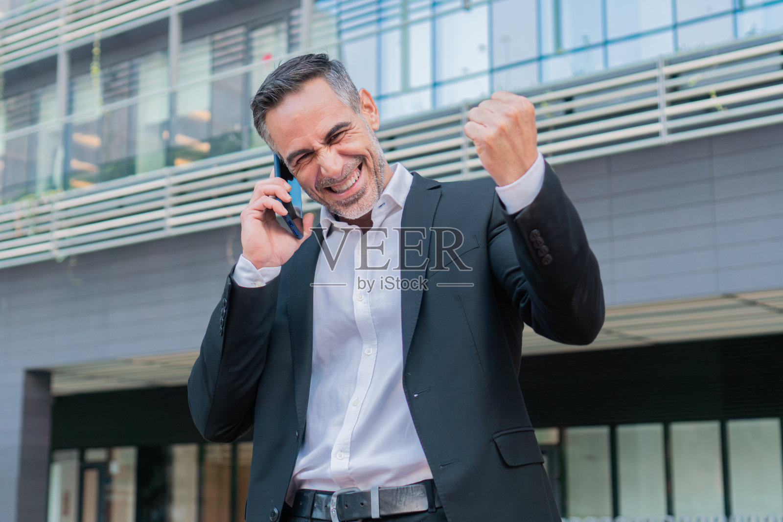 商人用智能手机聊天，对着镜头微笑着庆祝自己的成就。中年成年经理心情很好，收到了好消息。商务人士用手机聊天，心情愉快照片摄影图片