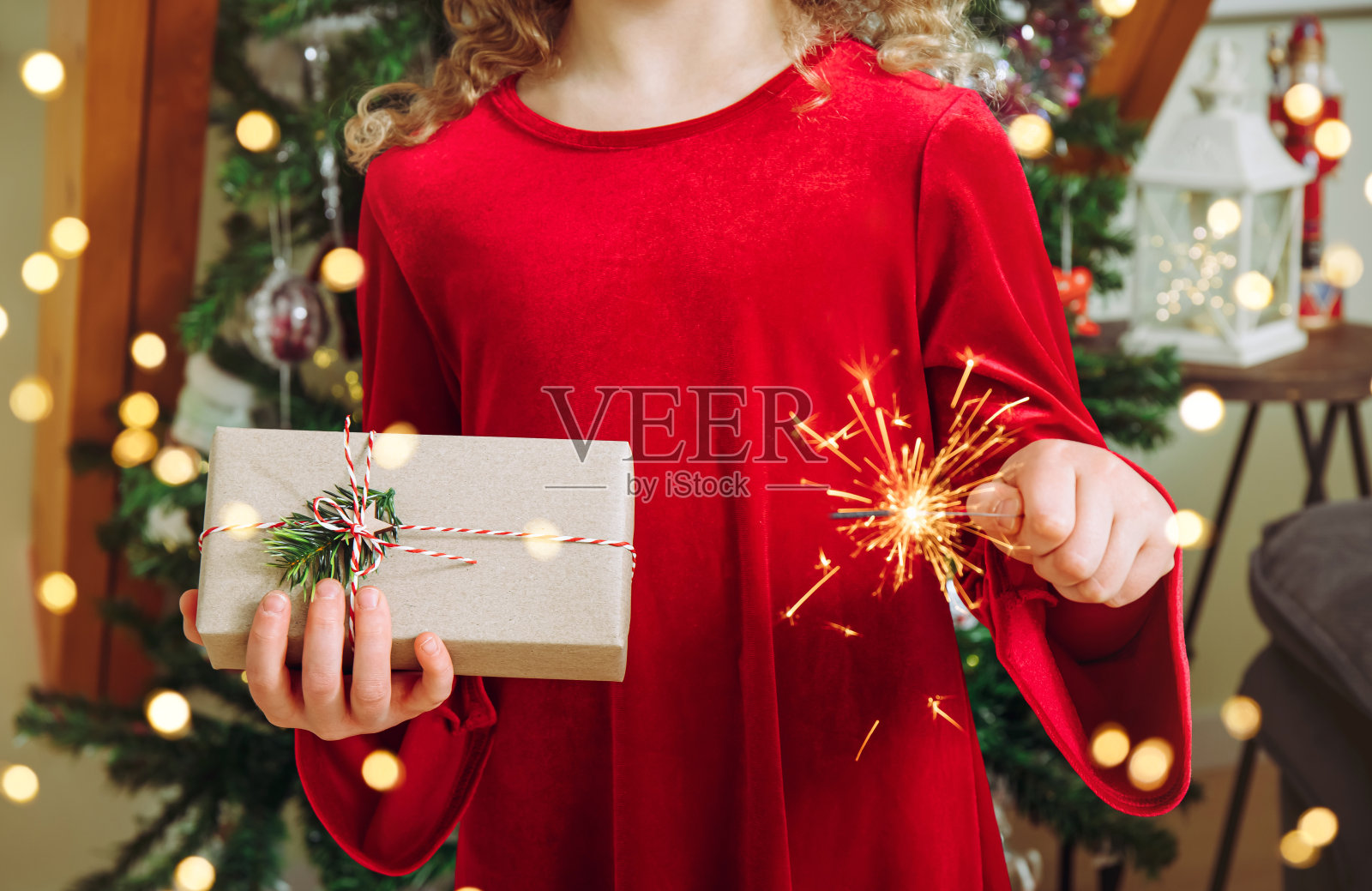 小女孩在家里拿着圣诞礼物，手里拿着闪亮的蜡烛。平安夜庆祝活动。照片摄影图片