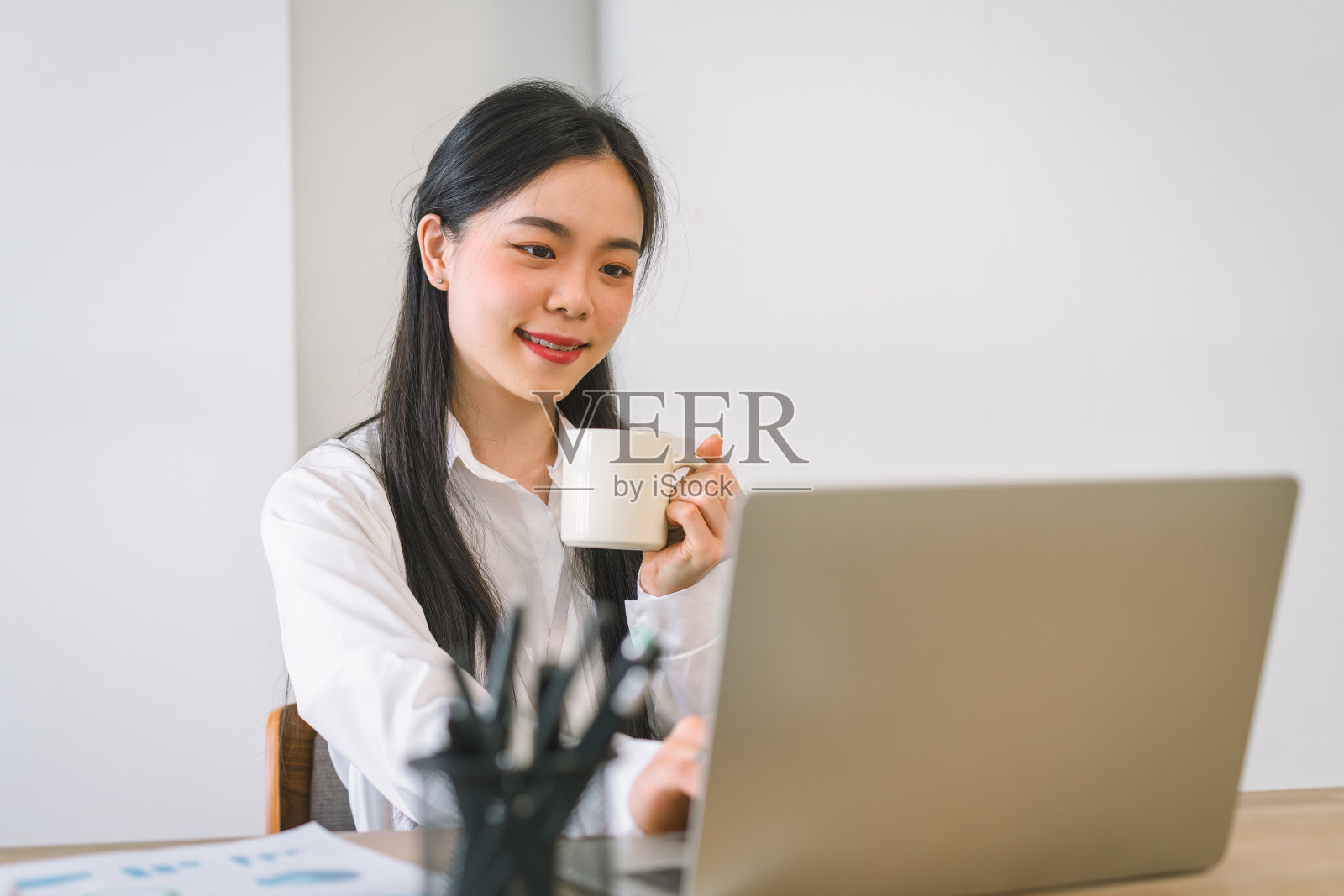 成功的亚洲女商人在办公室用笔记本电脑工作时看起来自信而微笑。照片摄影图片