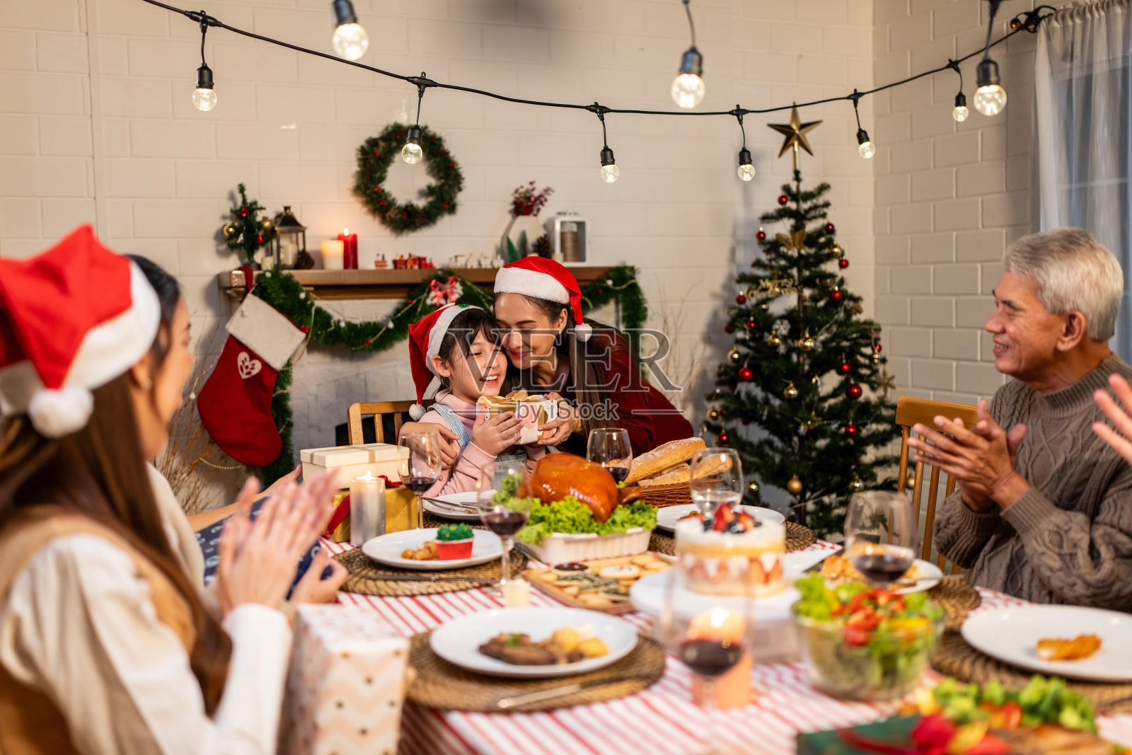 亚洲家庭在圣诞晚会上给小女儿送礼盒。漂亮的小女孩在吃饭时收到亲戚的礼物，一起在餐桌上庆祝节日感恩节照片摄影图片