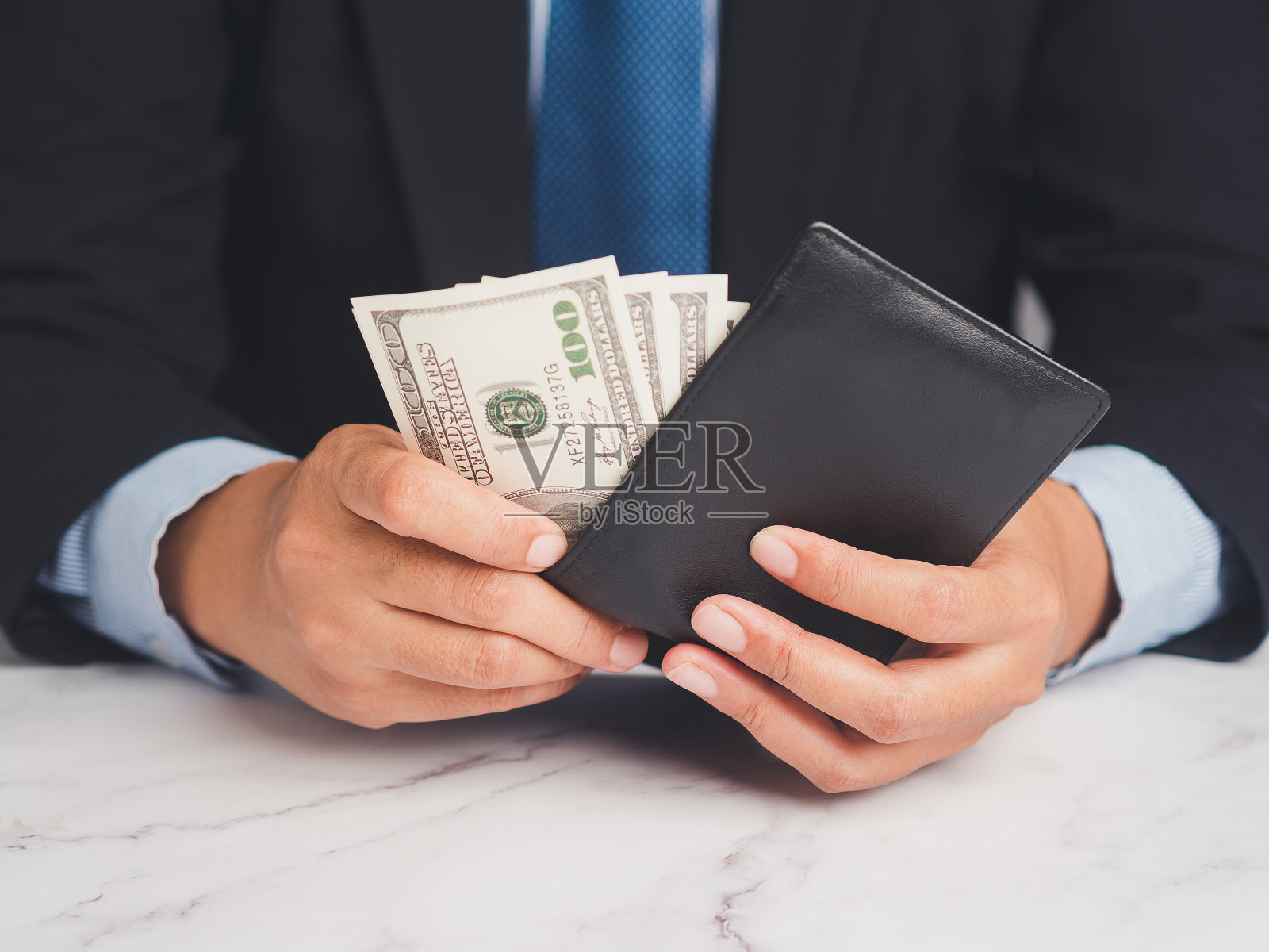 商人坐在桌旁，手里拿着一个装有美元钞票的钱包照片摄影图片