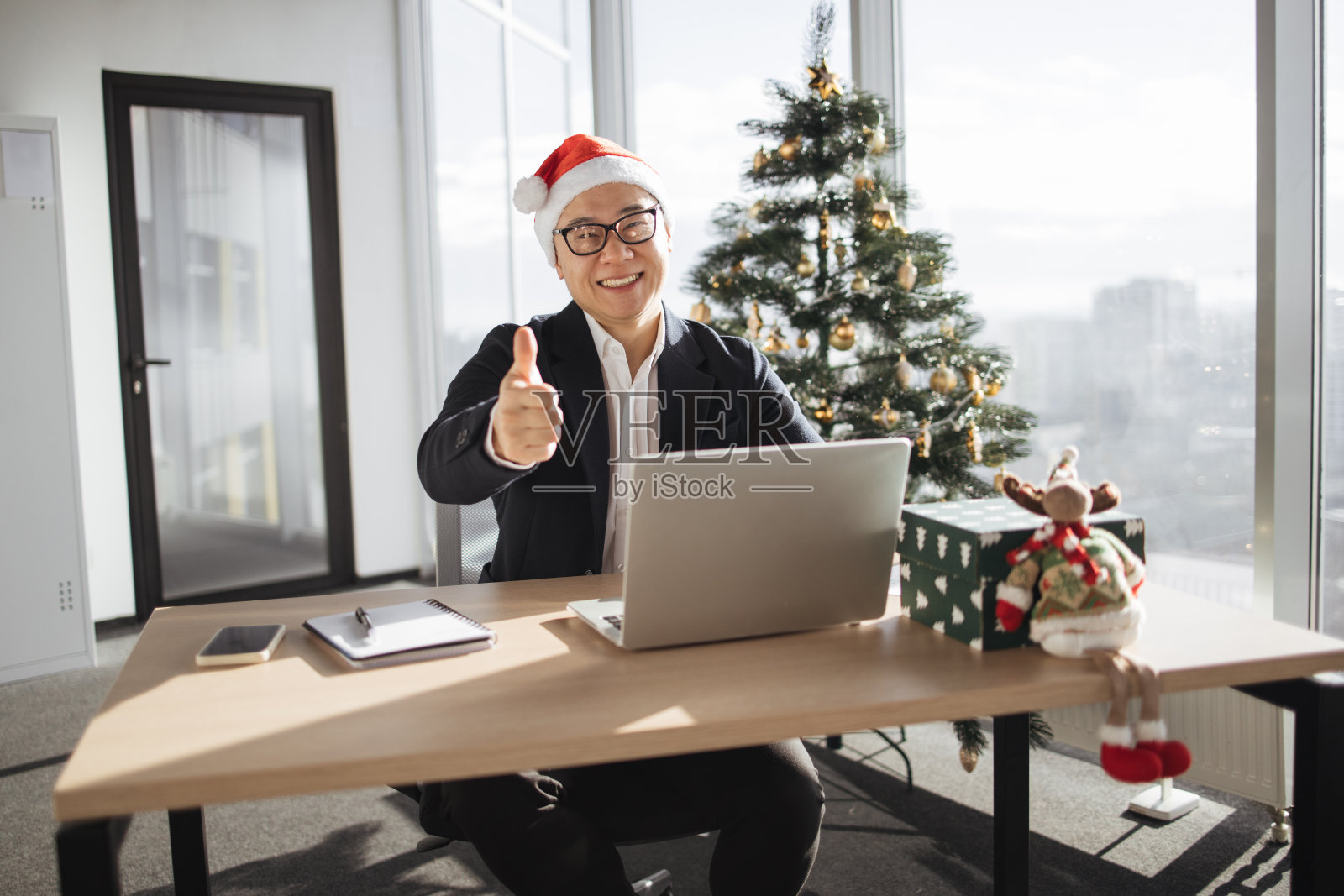 商人坐在圣诞树旁的办公室里用笔记本电脑工作照片摄影图片