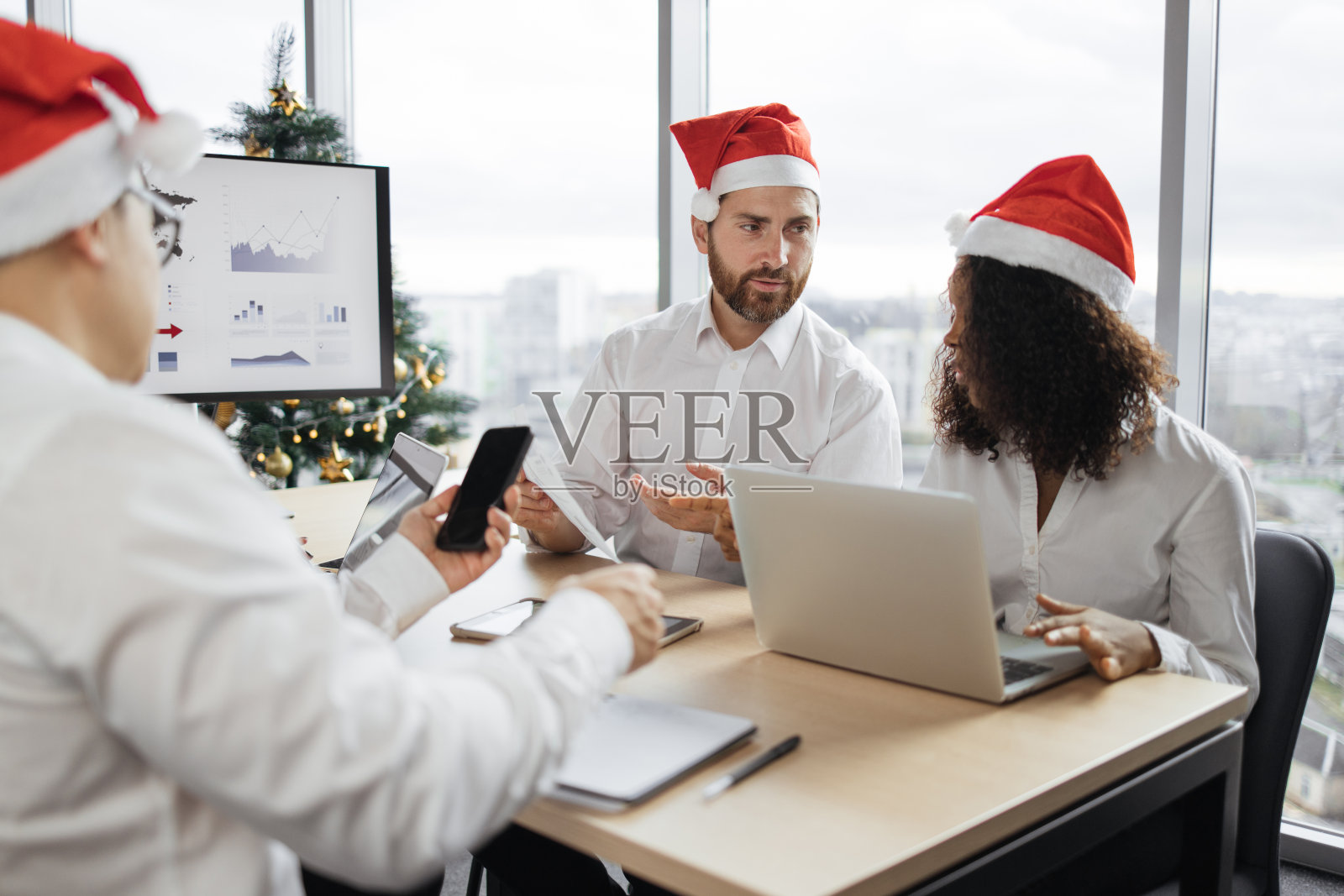 一个商人和他带着圣诞帽的男女同事坐在桌子旁照片摄影图片