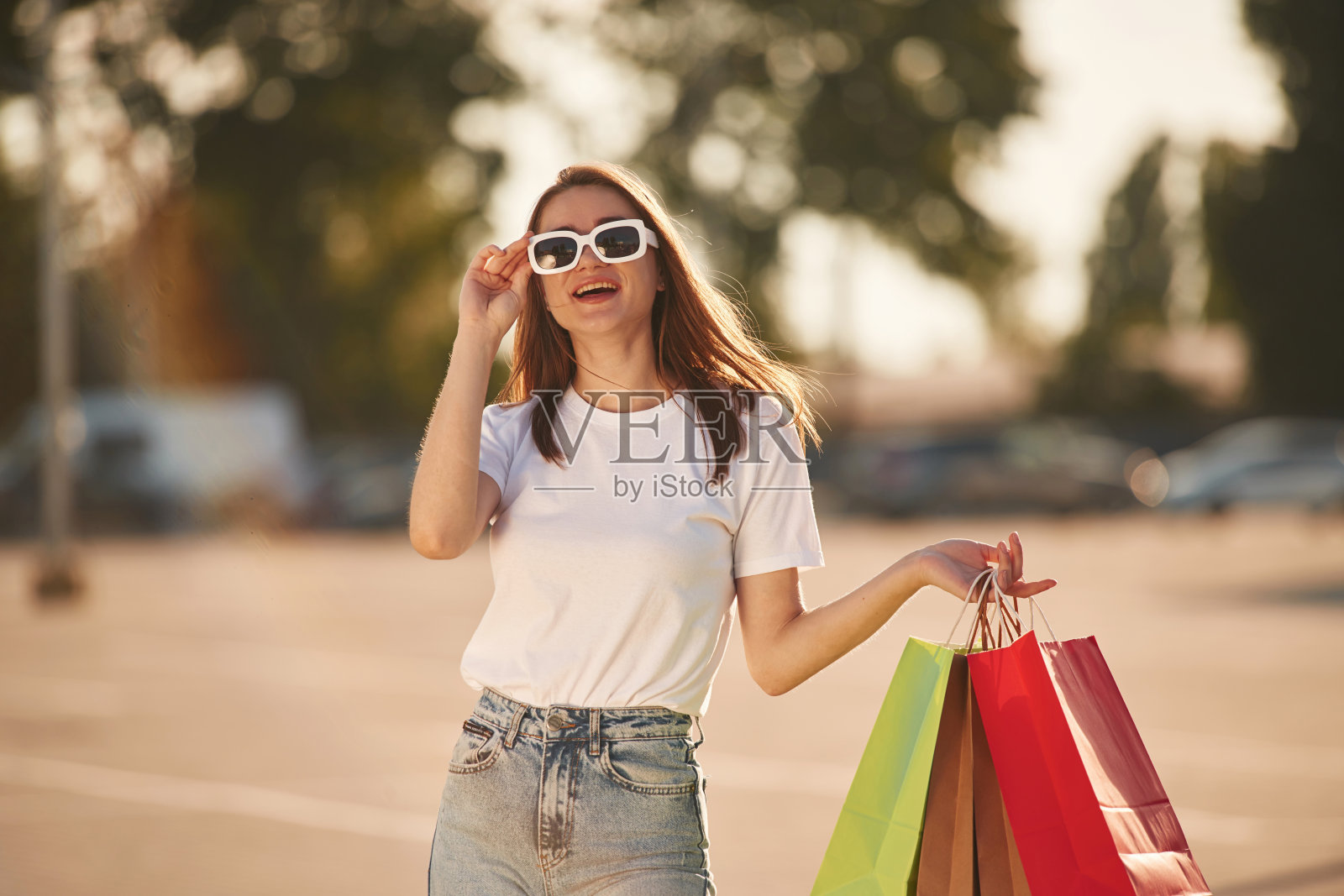 戴着墨镜，站着。穿着便服的美女在户外拎着购物袋照片摄影图片