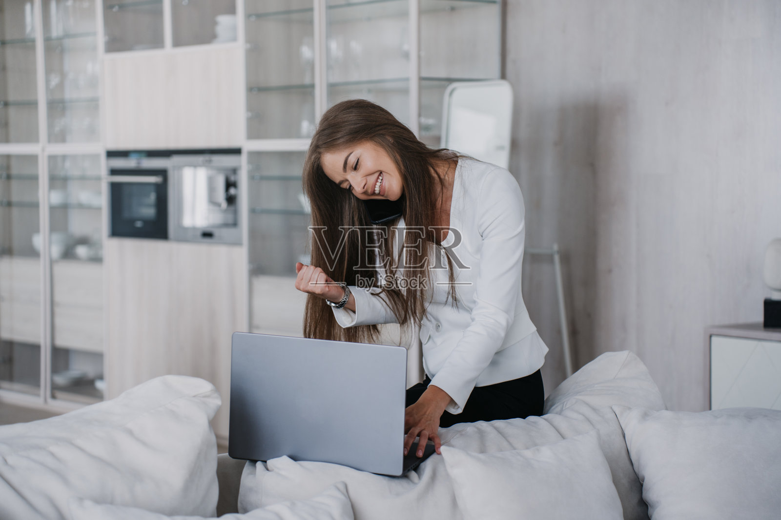 穿着白色夹克的开朗的白人年轻女商人坐在舒适的沙发上用笔记本电脑打视频电话，用紧握的拳头微笑警告丈夫。成功女性在家通过网络聊天。照片摄影图片