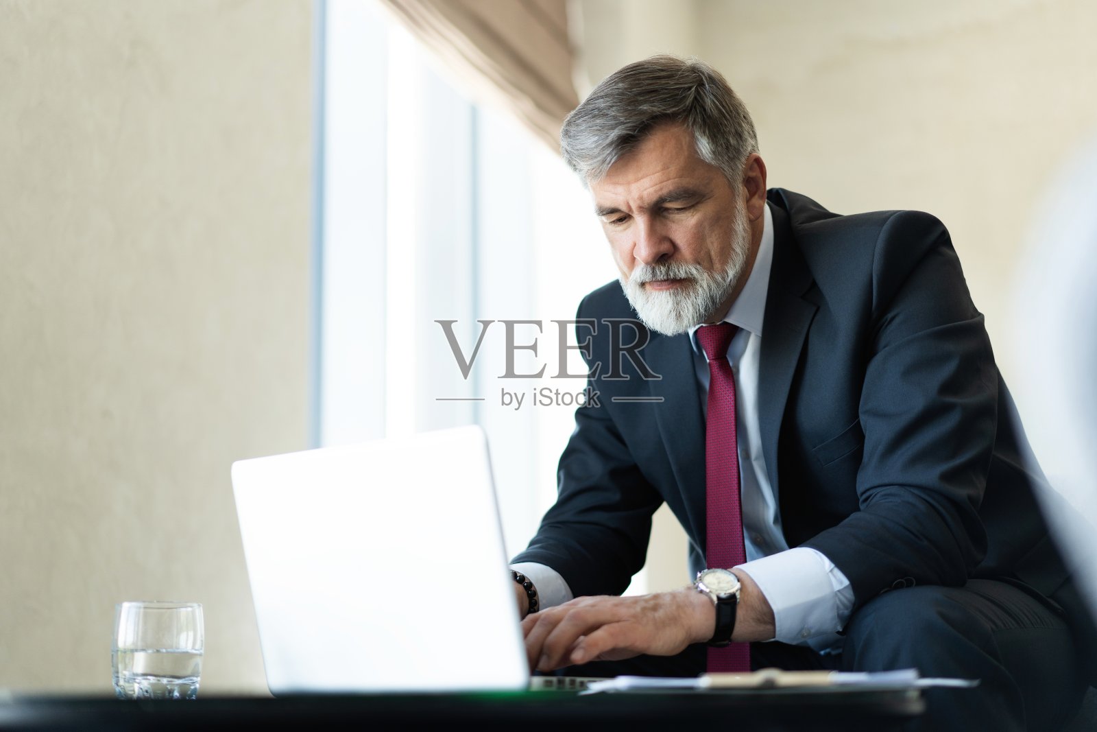 成熟的商人在笔记本电脑上工作。帅气成熟的商业领袖坐在现代化的办公室里。照片摄影图片