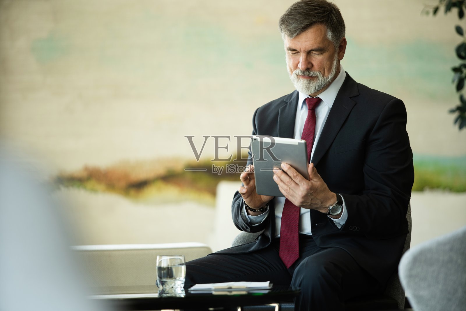 有思想、微笑、成熟的商人拿着平板电脑坐在办公室里。照片摄影图片