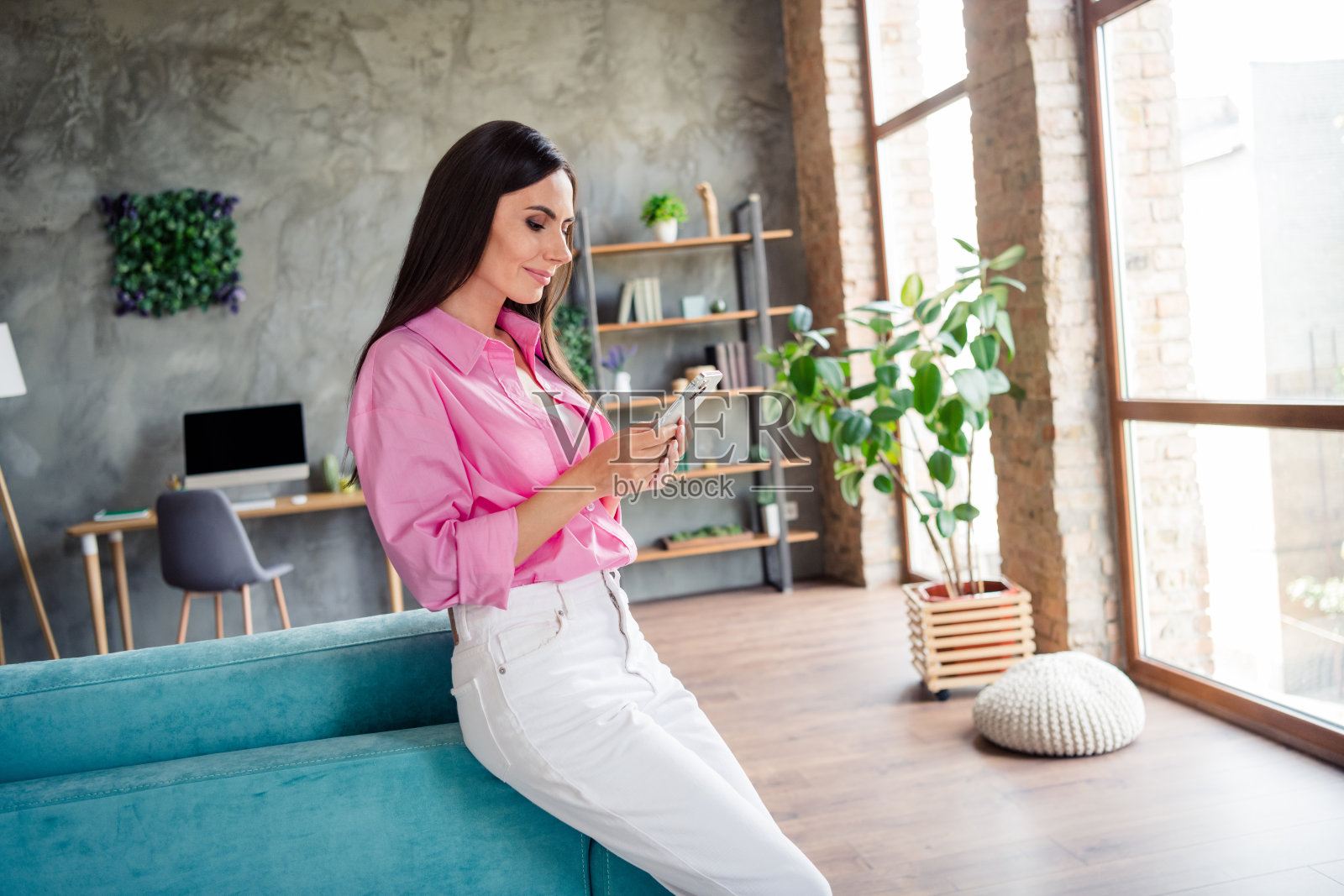 可爱的积极的年轻女士穿着粉红色的衬衫在室内键入苹果iphone三星现代设备的照片照片摄影图片