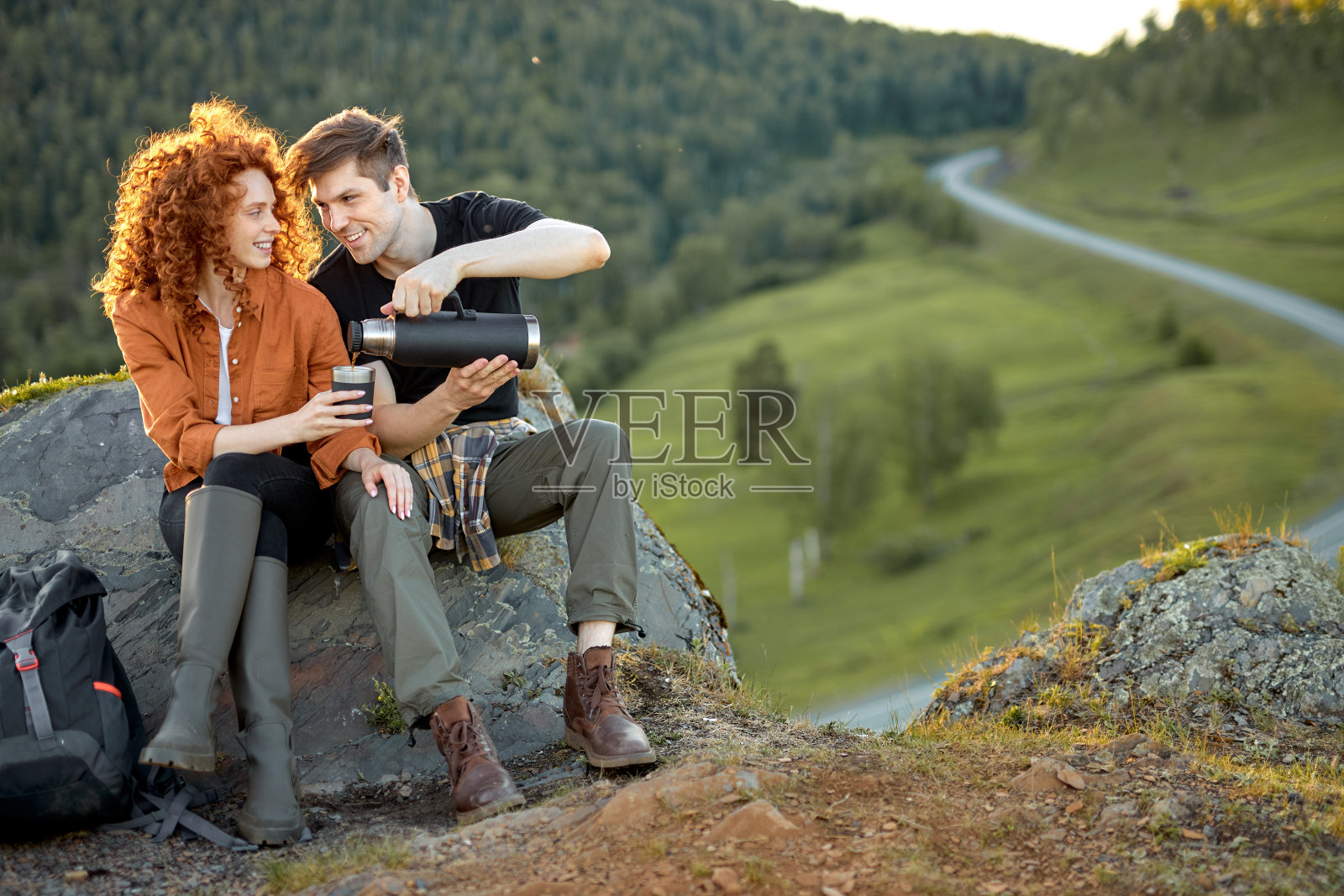 一对年轻的情侣坐在乡下的岩石上喝茶照片摄影图片
