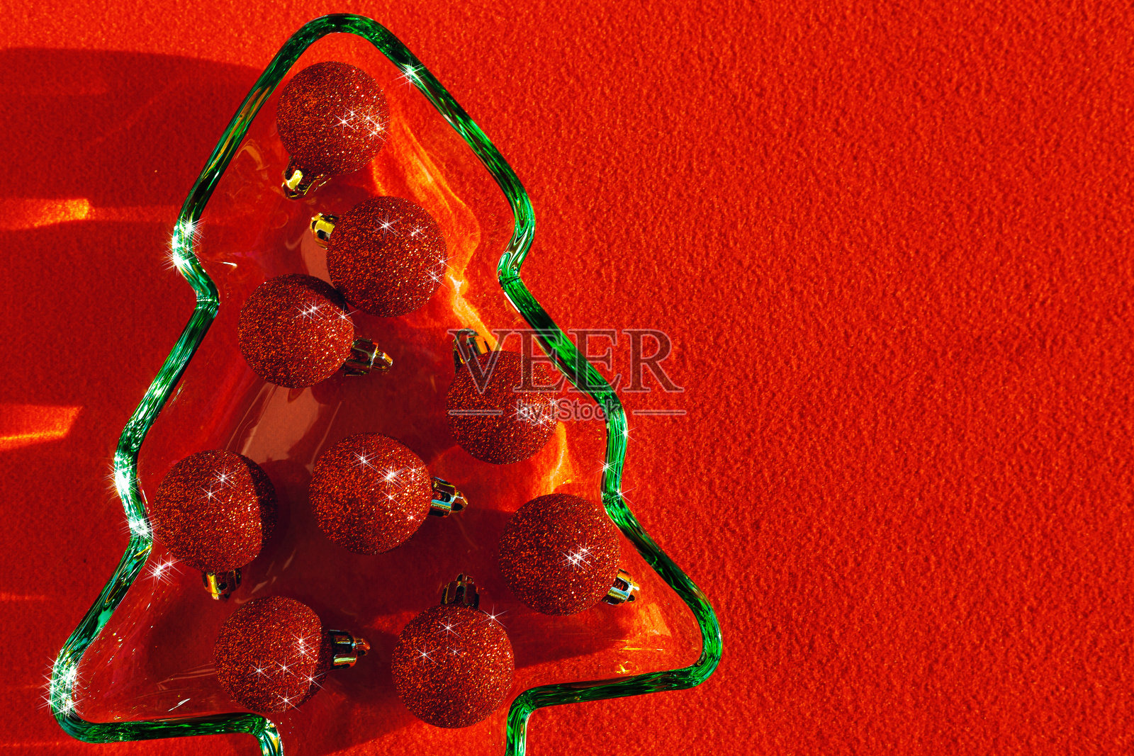 红色背景下的阳光下，绿色的玻璃板上缀着闪闪发光的红色圣诞球，而不是食物。寒假晚餐概念，简约风格，明星滤镜，特写照片摄影图片