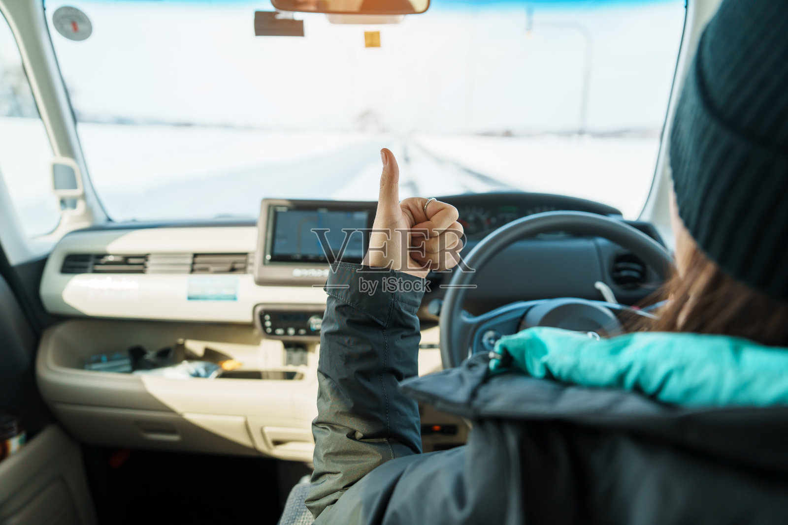 快乐的旅行者在雪地上开车，手指向上，冬季女游客在车里欣赏雪林景色。冬季旅游，自驾游，探索和度假的概念照片摄影图片