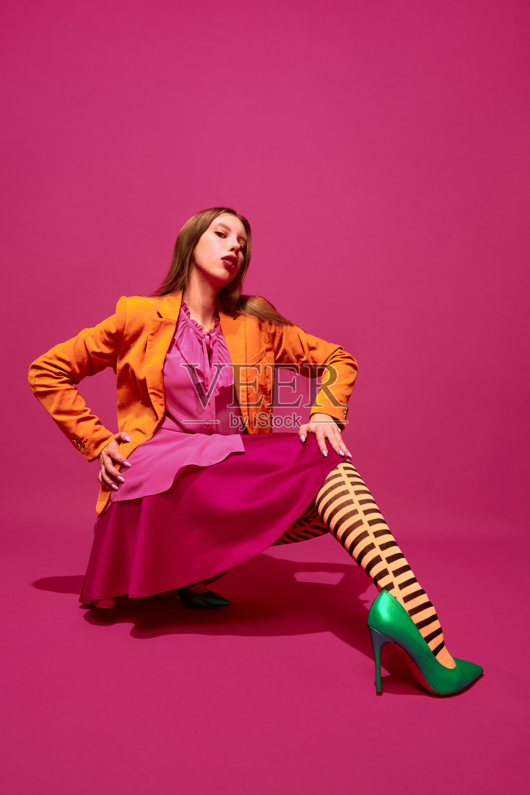 年轻女孩的全身肖像，女士在不寻常的，杂色橙色条纹紧身衣，长裙和短夹克洋红色工作室的背景。照片摄影图片