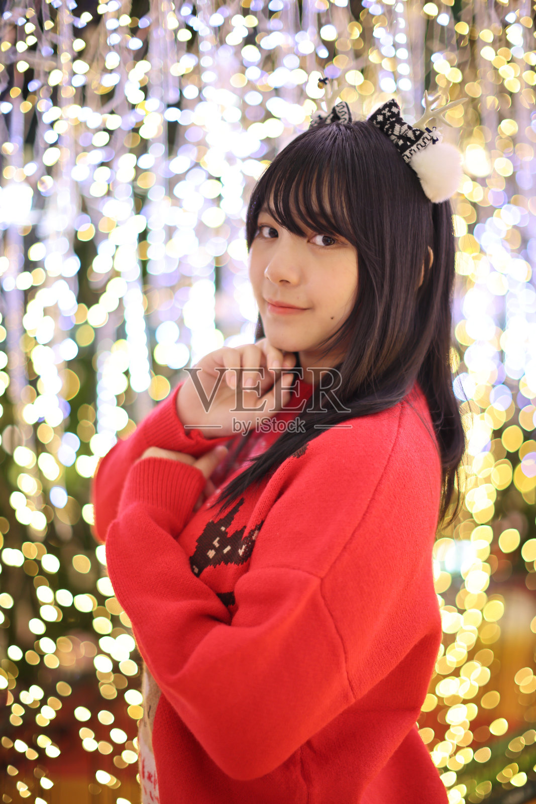 漂亮的亚洲年轻女子穿着一件红色毛衣，上面挂着圣诞树灯照片摄影图片