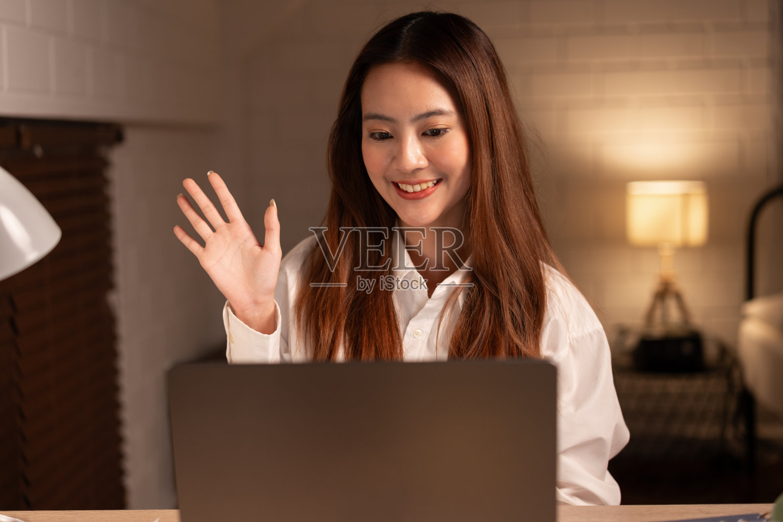 快乐的亚洲少女晚上在家用笔记本电脑视频通话和挥手照片摄影图片