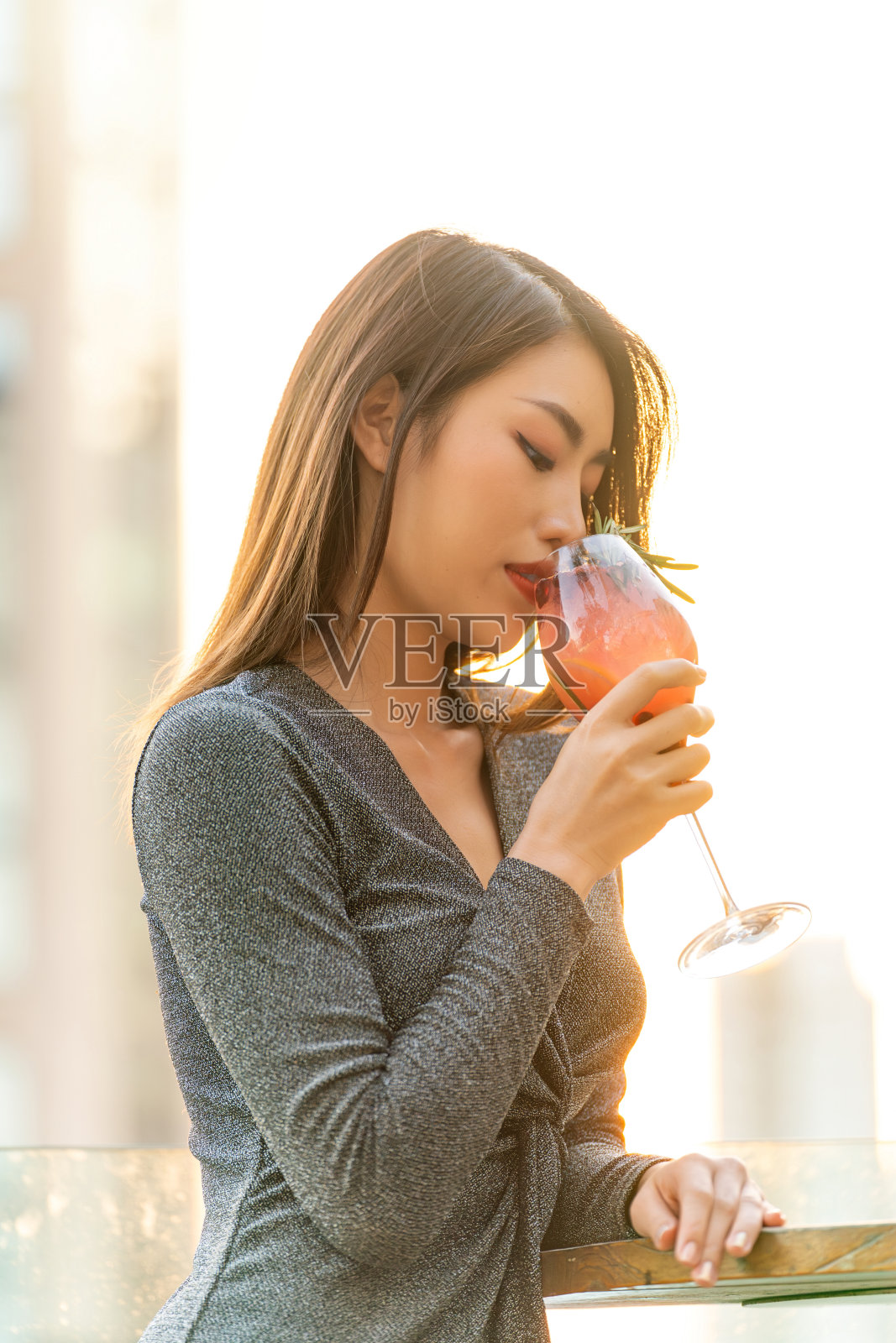 在温暖的晚霞中，一个亚洲女人在屋顶酒吧喝鸡尾酒照片摄影图片
