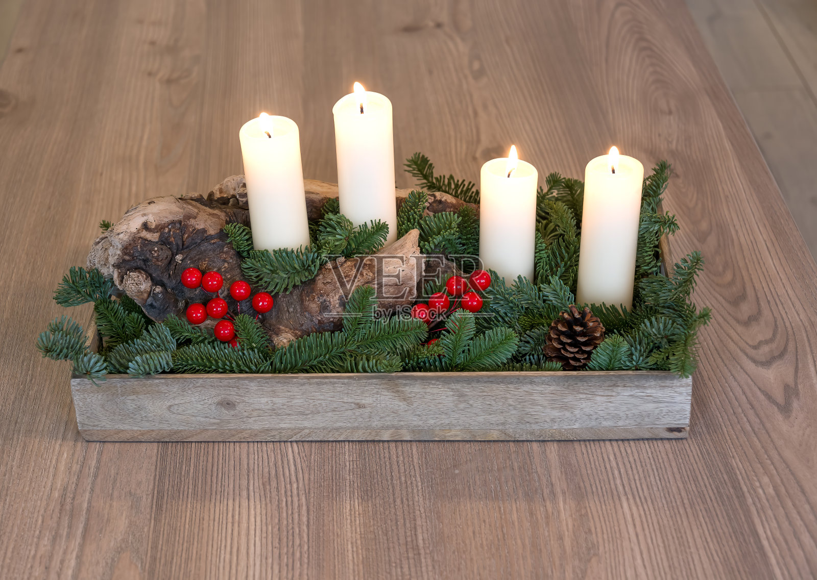 这是一个手工制作的降临节或圣诞节构图的例子，有四支燃烧的蜡烛，在一个老树干上，周围是绿色的云杉树枝和红色的浆果。降临节、圣诞节和新年的概念。照片摄影图片