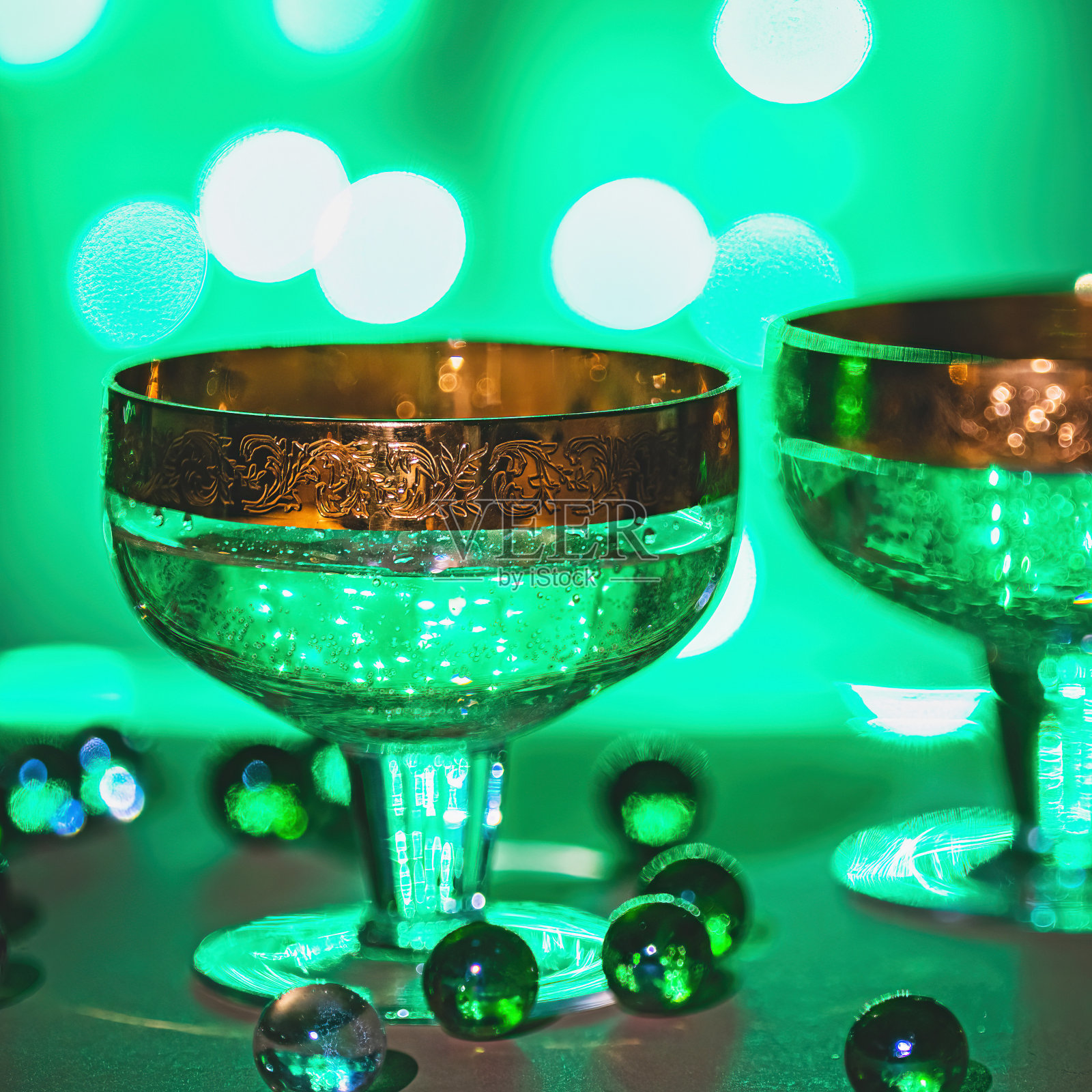 装有香槟和圣诞装饰品的玻璃杯，后面的圣诞灯是淡绿色的。照片摄影图片