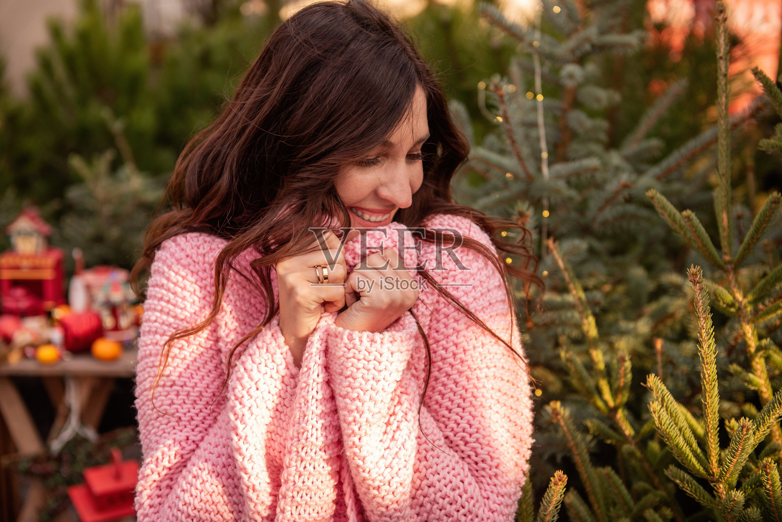 漂亮的年轻女子穿着粉红色针织毛衣，把自己裹得严严的，卷发在风中飘动照片摄影图片