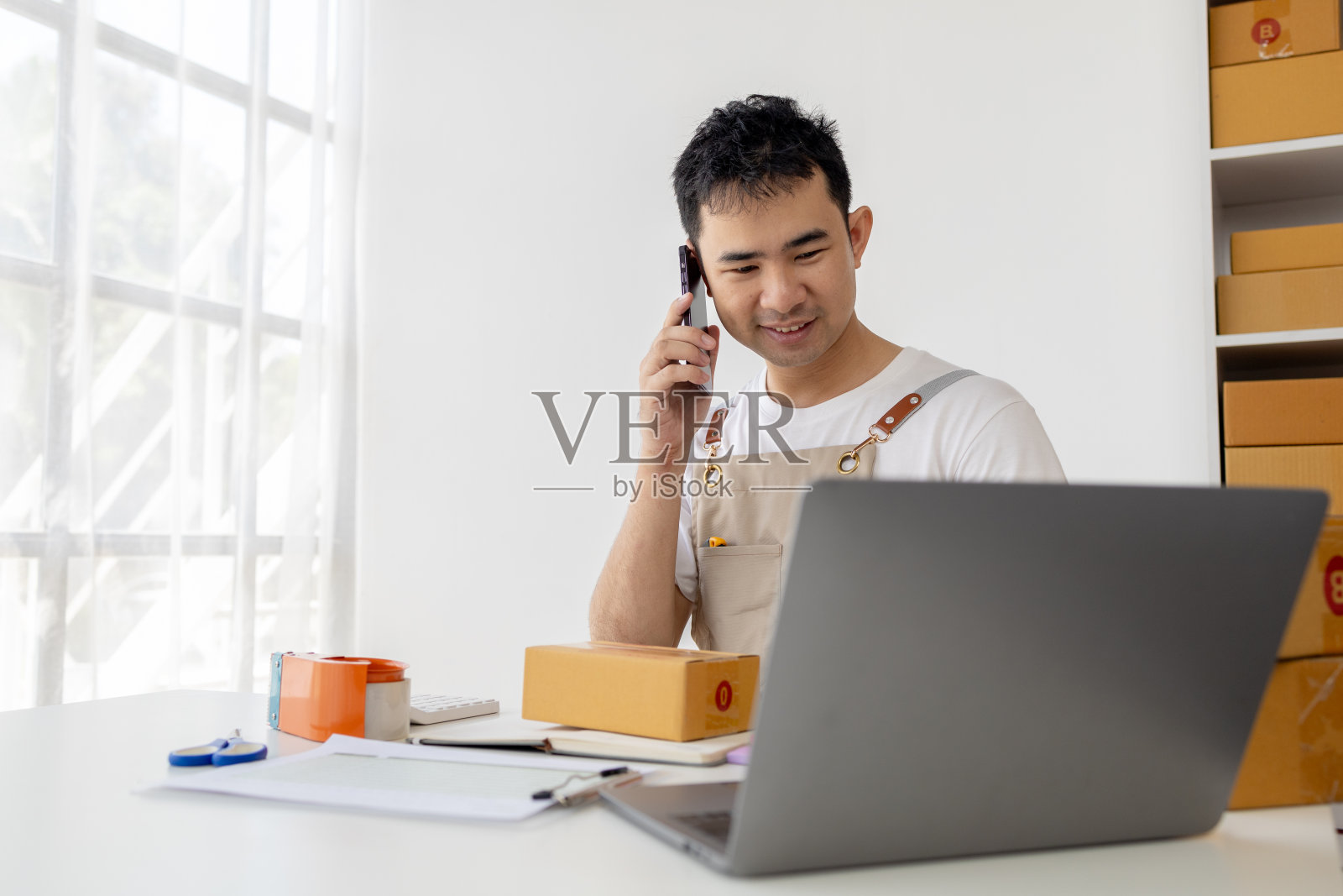 这个人正在与客户打电话，在网上销售产品，包装客户通过网上购物网站下订单的订单。网上销售产品和电子商务的概念照片摄影图片