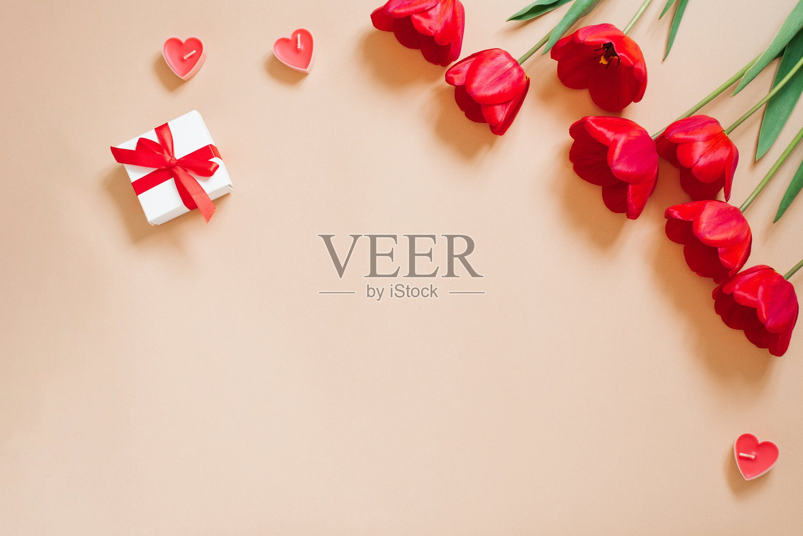 情人节浪漫背景。红色郁金香，带蝴蝶结的礼物，米色背景上的蜡烛心，还有复制空间。平躺照片摄影图片