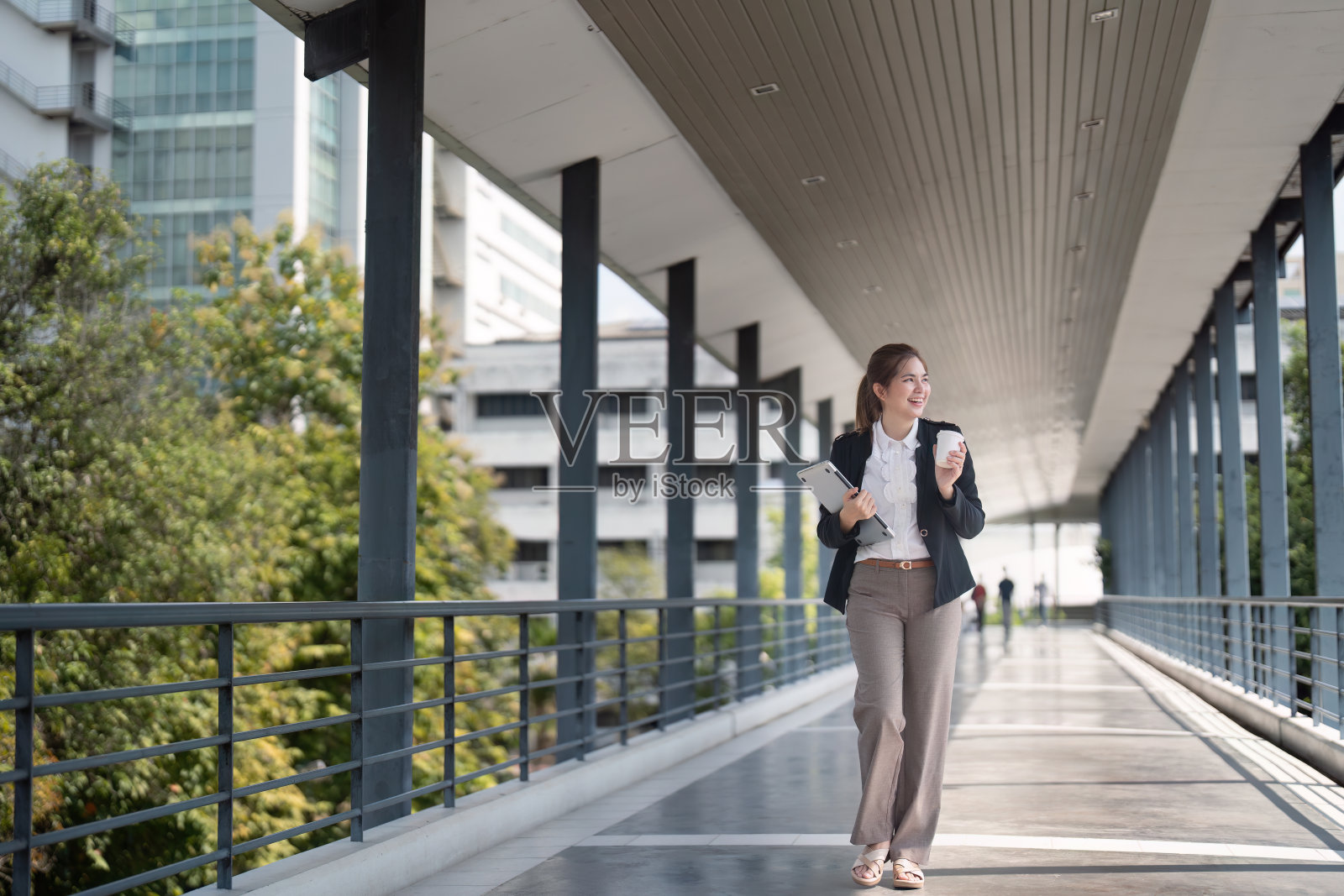 年轻的亚洲女商人开心自信地走在天桥上，同时去城市工作照片摄影图片