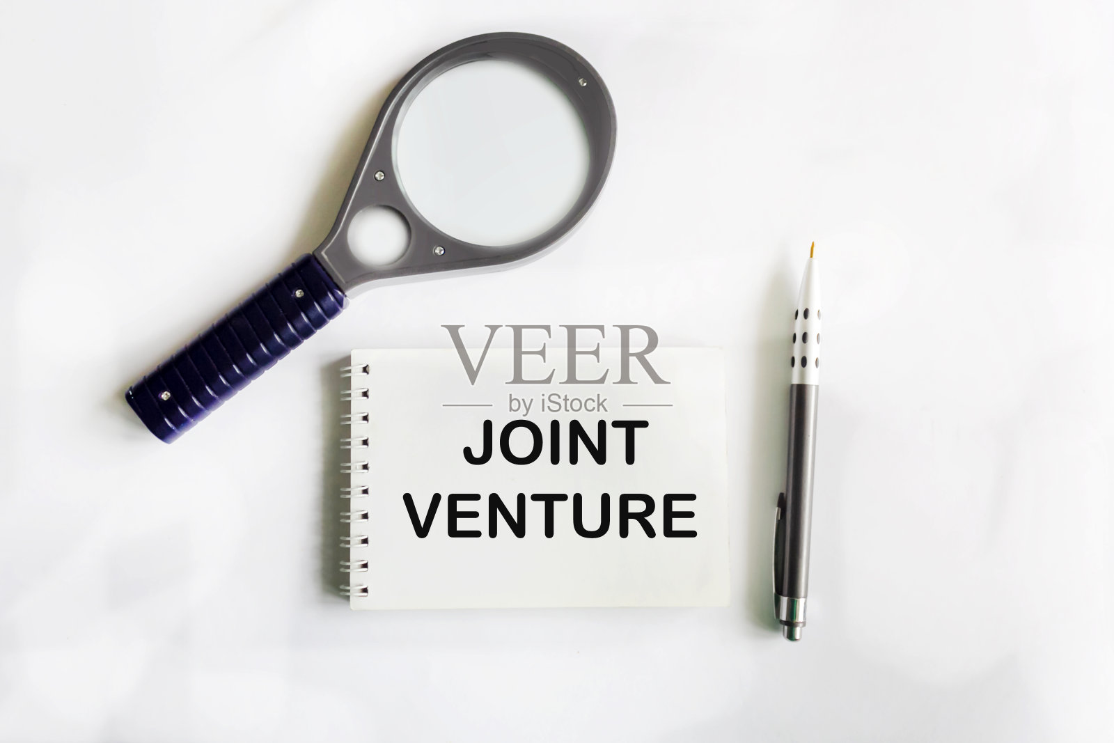 合资企业。白底记事本上的文字，旁边是放大镜照片摄影图片