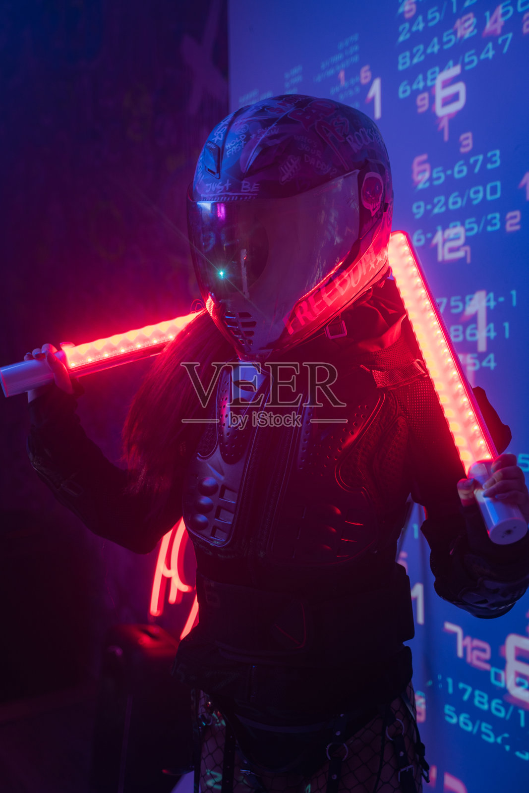 女人在未来的战术黑色西装和摩托车头盔与霓虹灯照片摄影图片