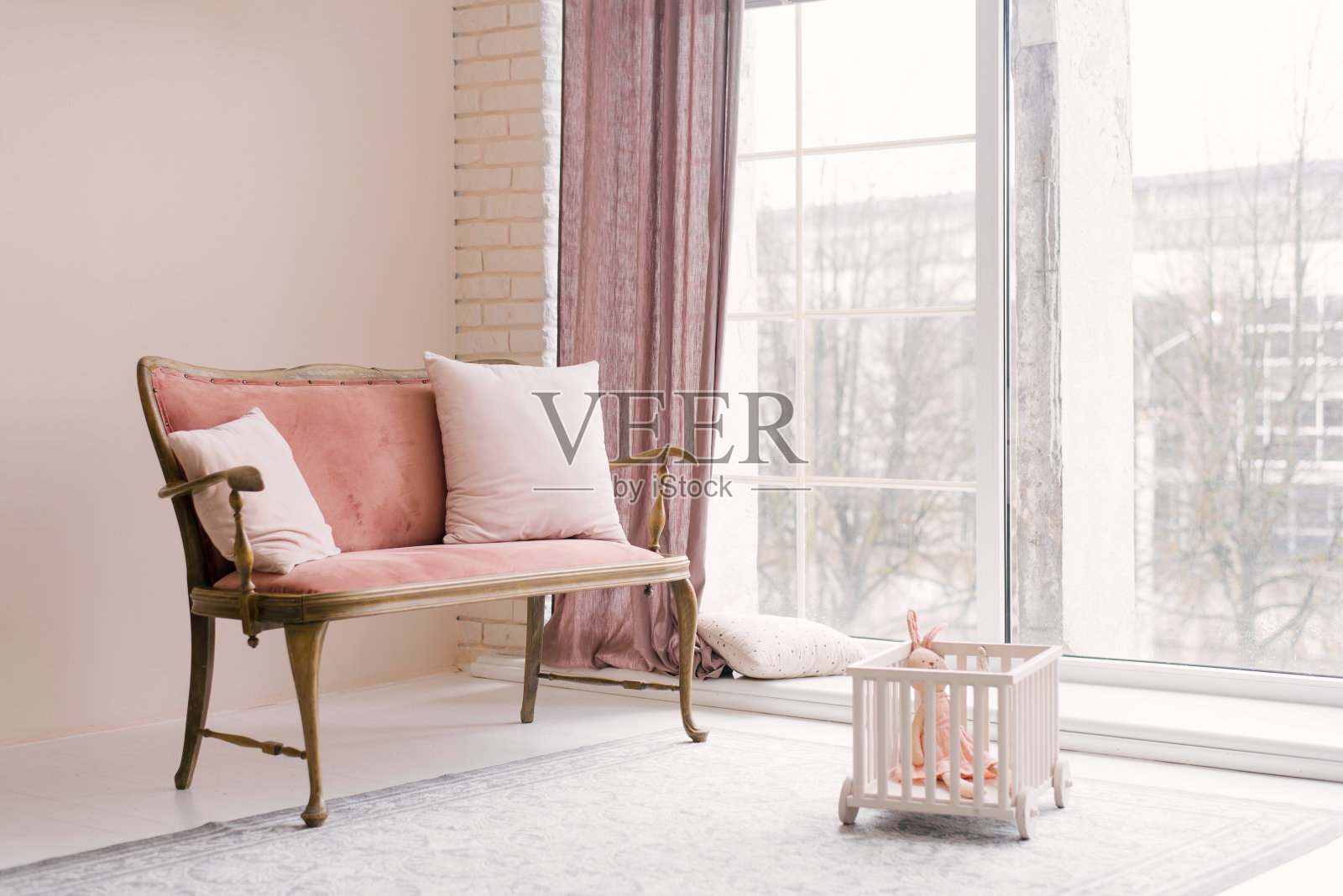 在客厅或孩子们的房间里，靠近窗户的地方放着一张带枕头的粉红色复古沙发。简约的室内设计照片摄影图片