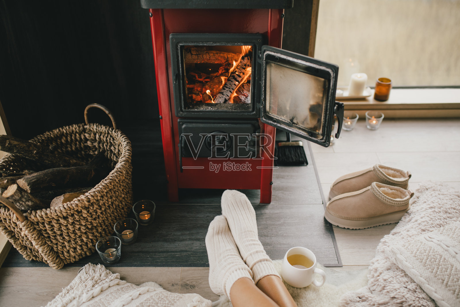 年轻女子穿着白袜子坐在壁炉旁，在舒适的小木屋里喝茶。照片摄影图片