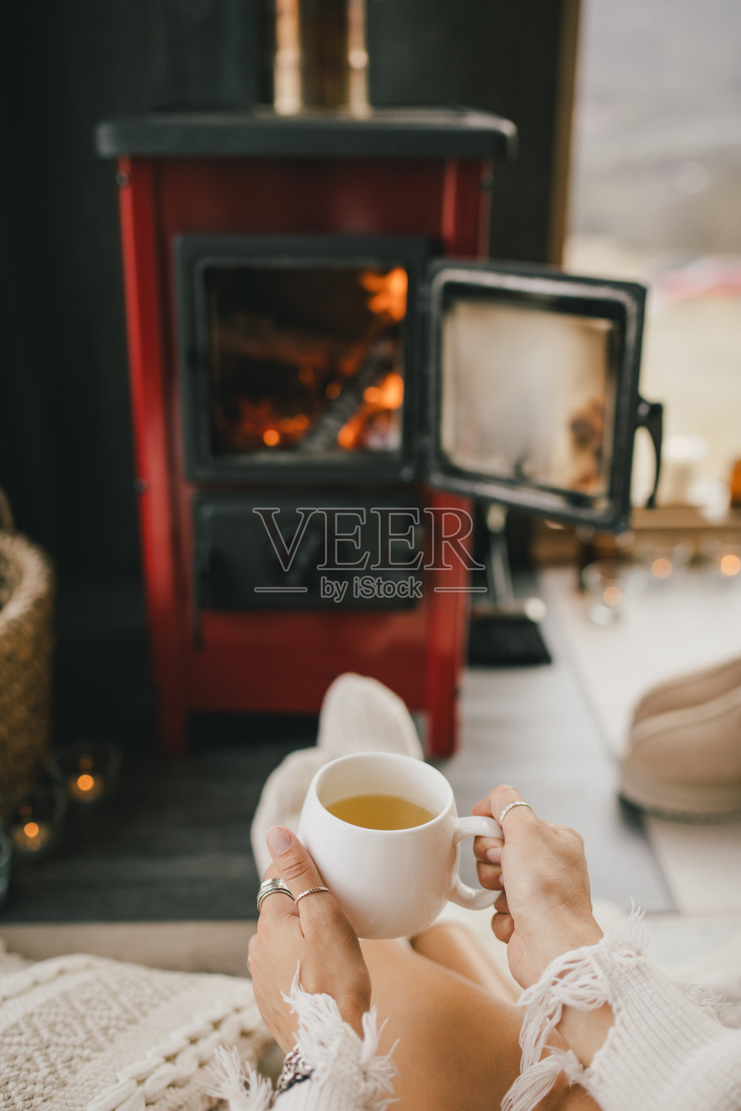 穿着白毛衣的年轻女子坐在壁炉旁，在舒适的小木屋里喝茶。照片摄影图片