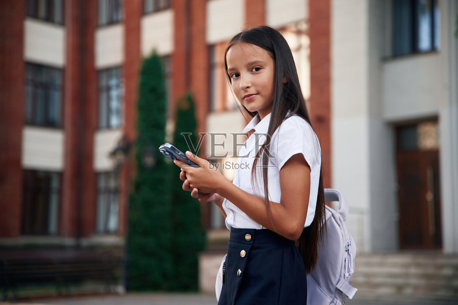 智能手机。穿制服的女学生在大楼附近的户外照片摄影图片