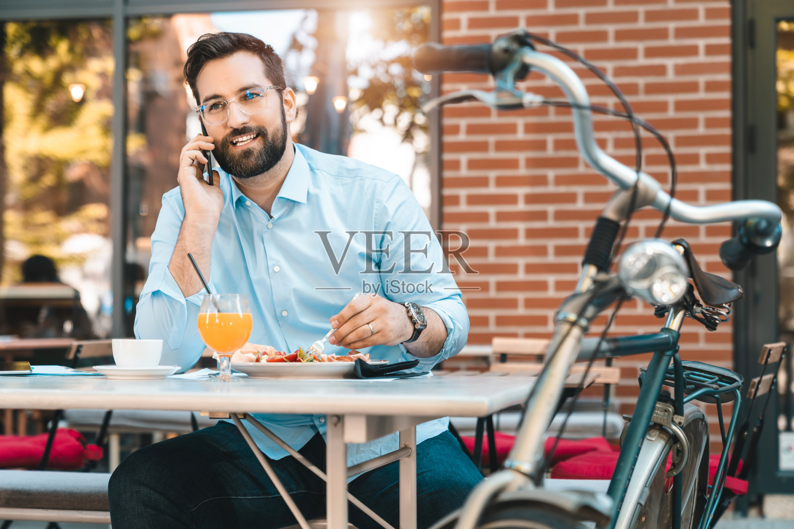 微笑的男企业家一边在餐厅吃早餐一边打电话照片摄影图片