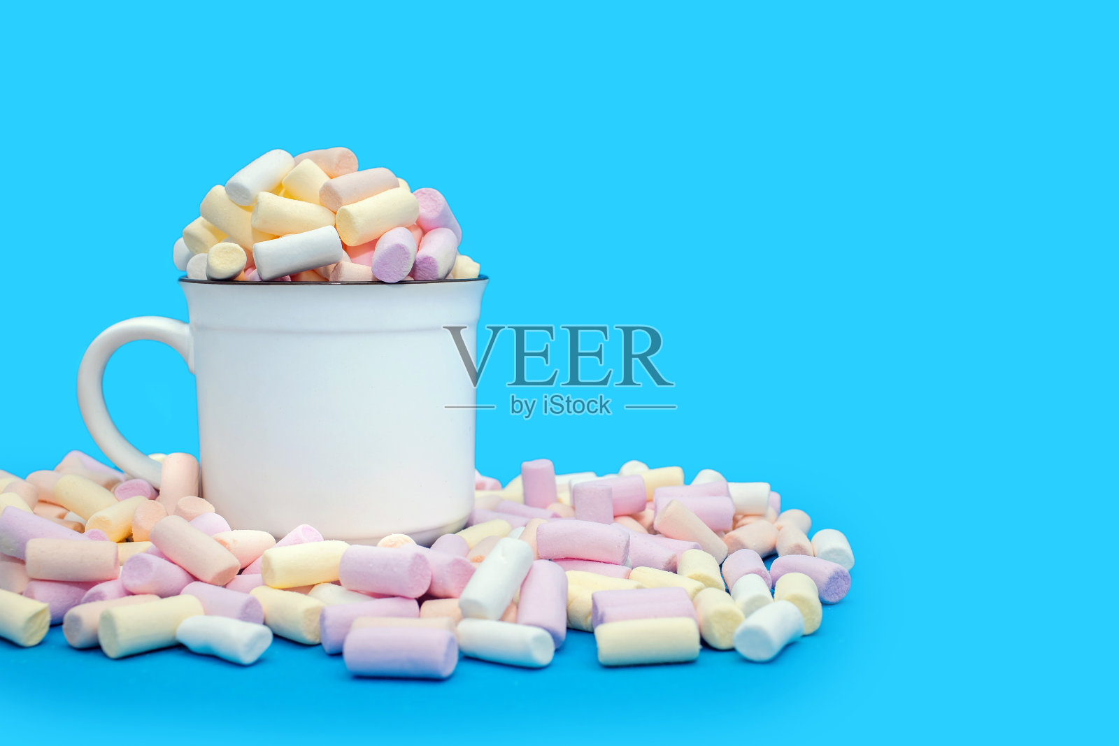 一个杯子，里面有可可或热巧克力，蓝色背景上撒着许多五颜六色的棉花糖照片摄影图片