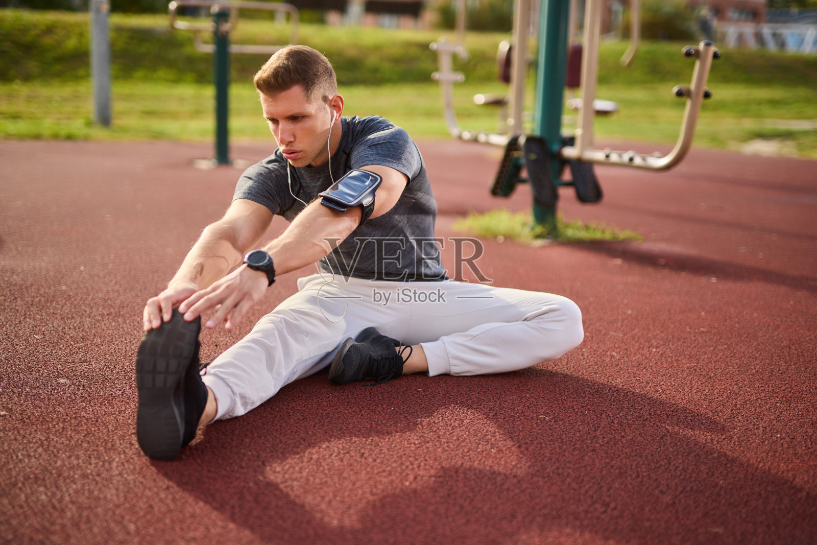 年轻的男运动员一边听音乐一边在户外伸展照片摄影图片