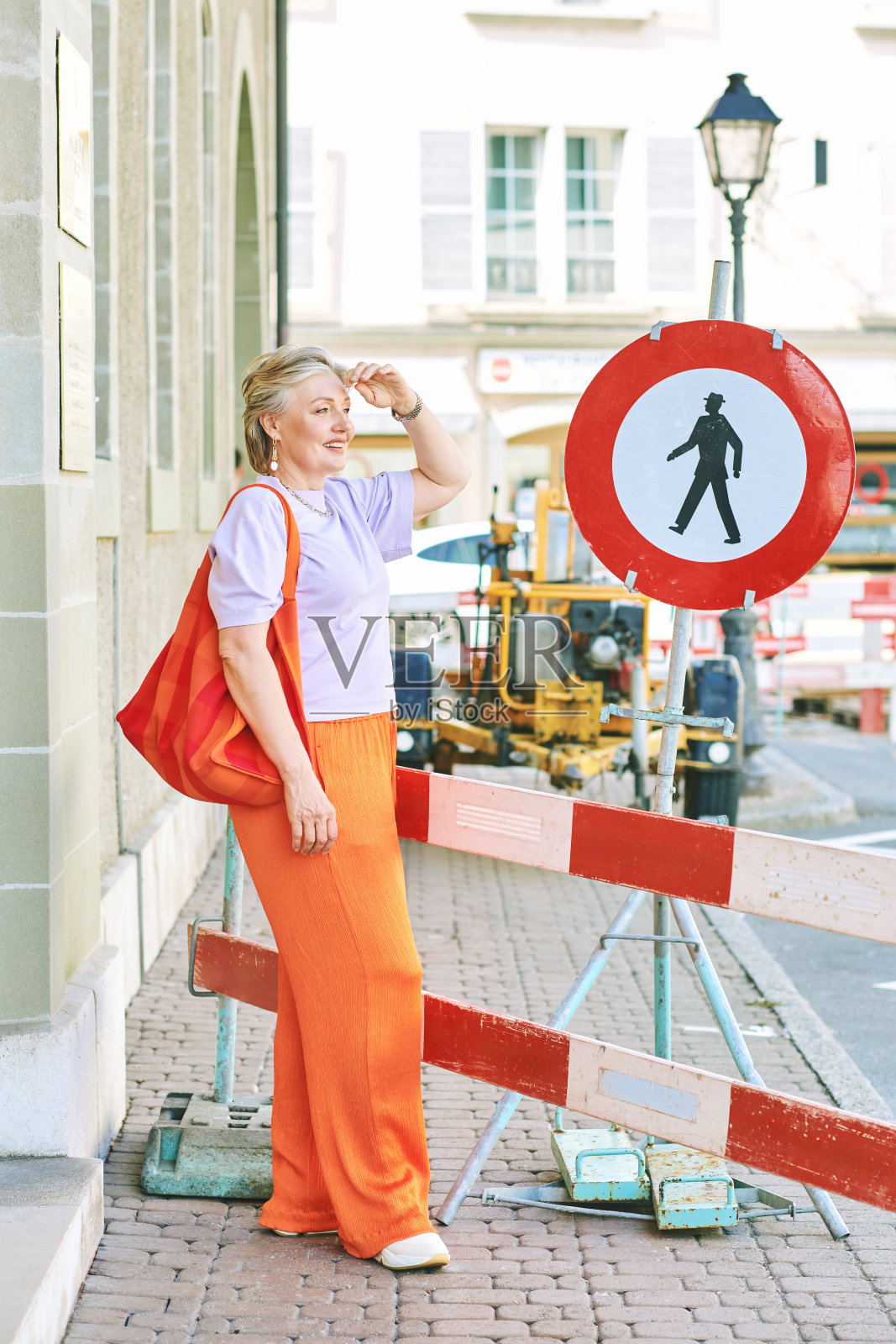 户外时尚肖像的时尚成熟的女人与灰色的头发，穿紫色上衣和橙色裤子照片摄影图片