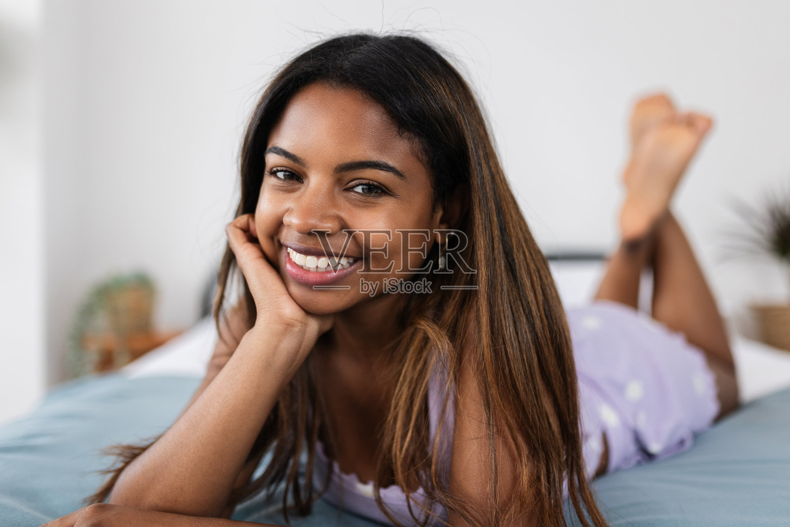 年轻的拉丁女子躺在家里的床上对着镜头微笑照片摄影图片