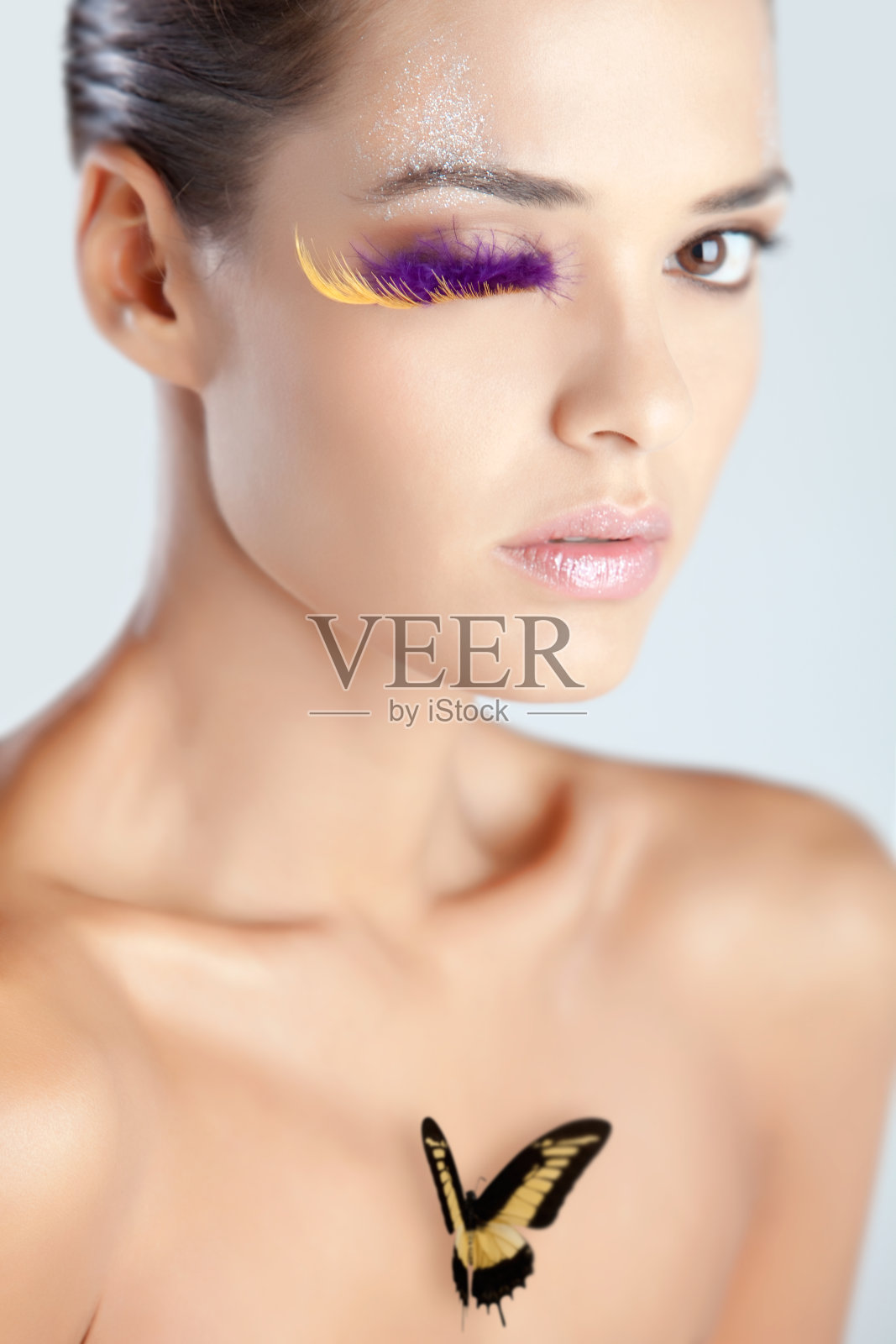 模特用紫色羽毛制成的假睫毛，闪亮的嘴唇上有蝴蝶的创意妆容照片摄影图片