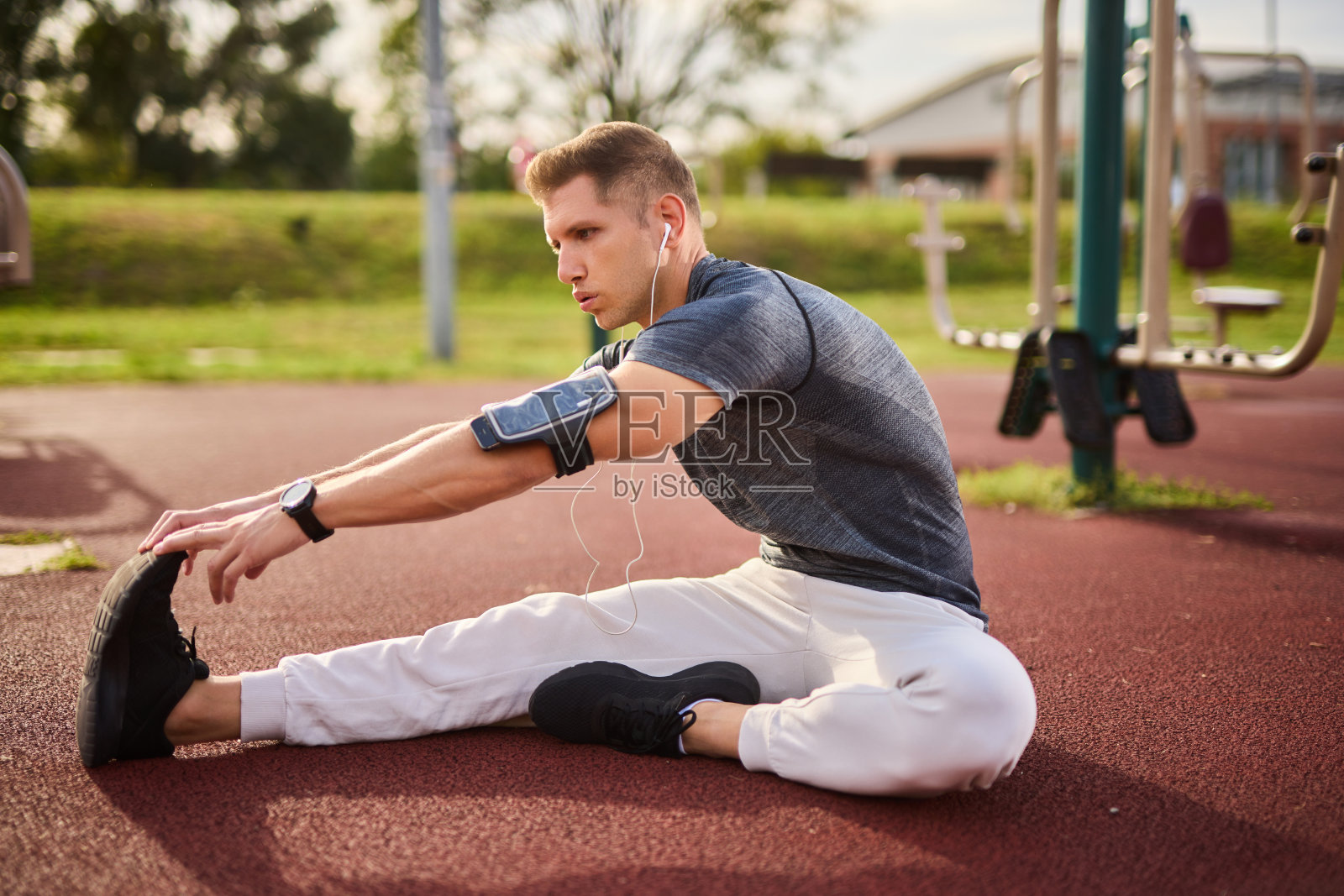 年轻的男运动员一边听音乐一边在户外伸展照片摄影图片