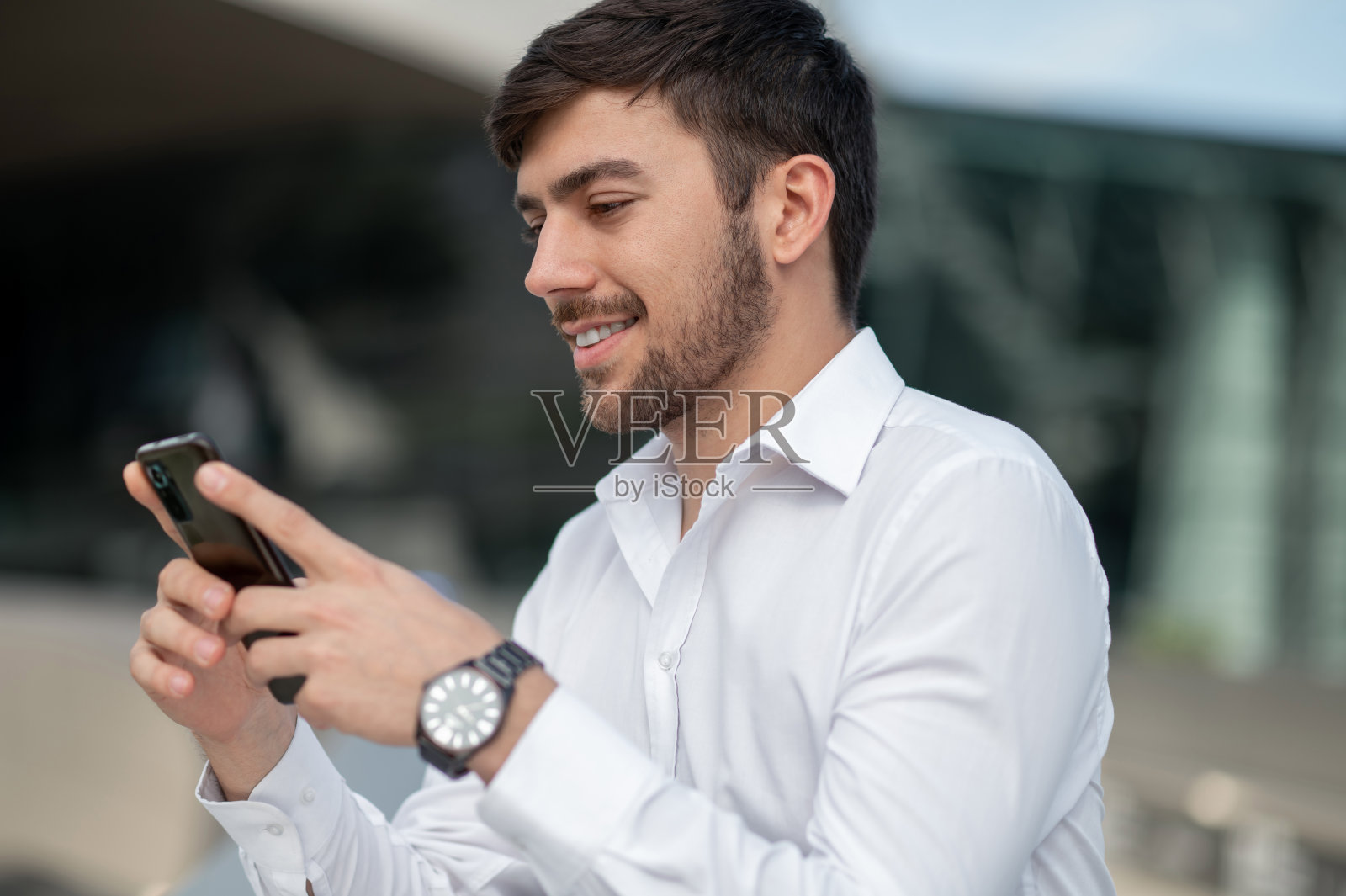 一个面带微笑的年轻人在电话里发短信照片摄影图片