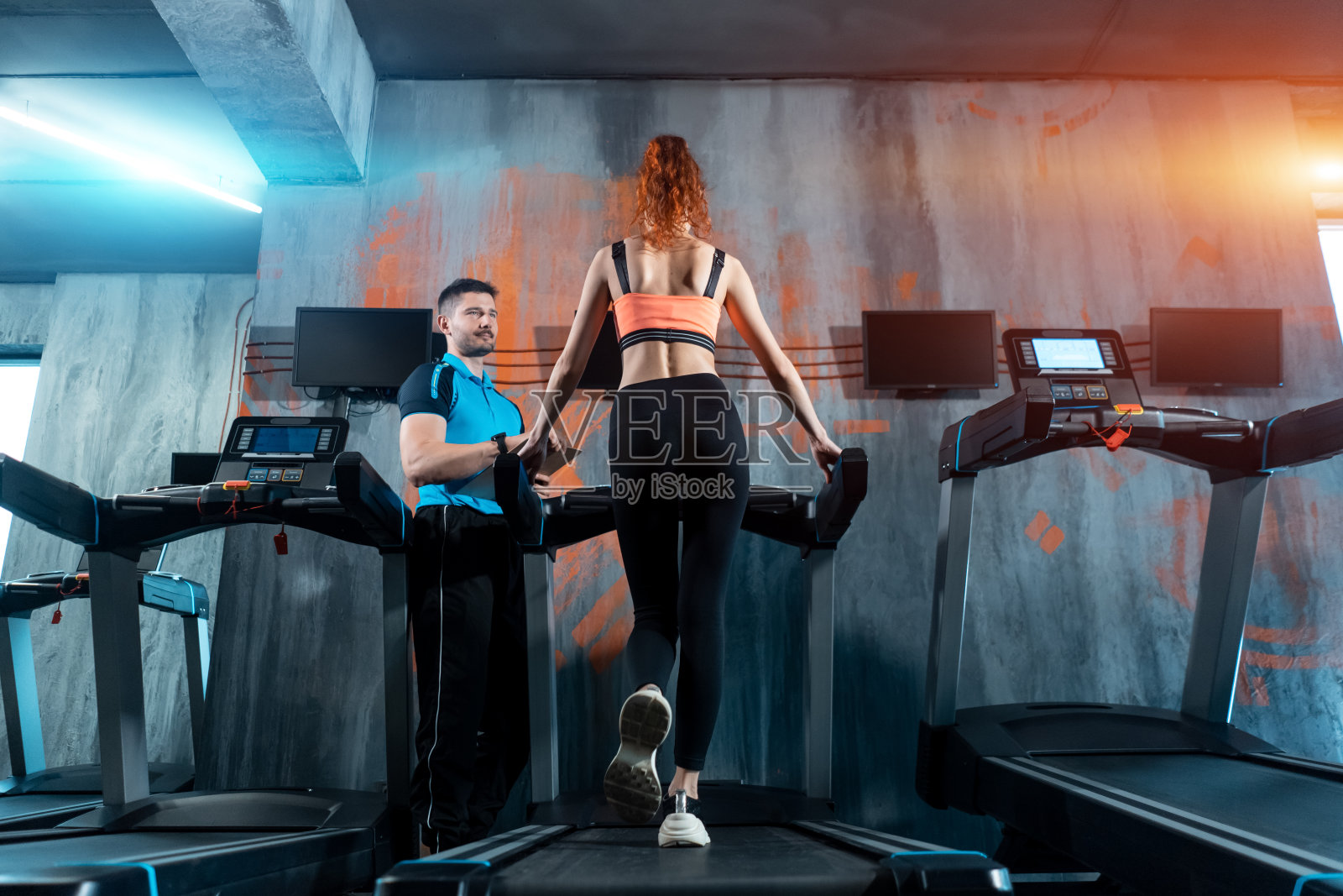 年轻漂亮的女人在跑步机上和私人教练一起跑步照片摄影图片